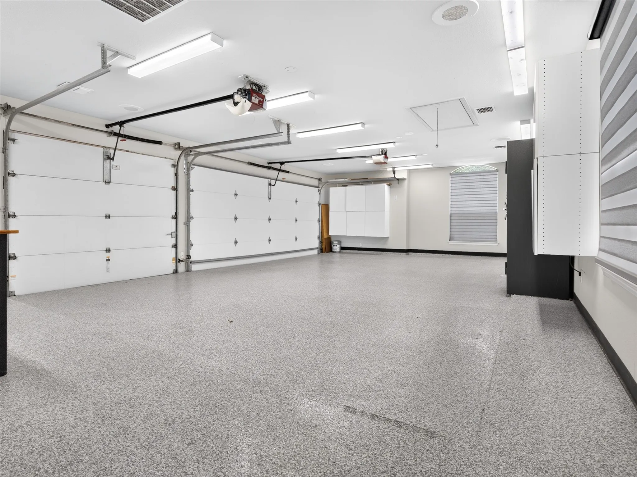 Two-car garage featuring segmented overhead doors, epoxy flooring, built-in cabinetry, and integrated lighting