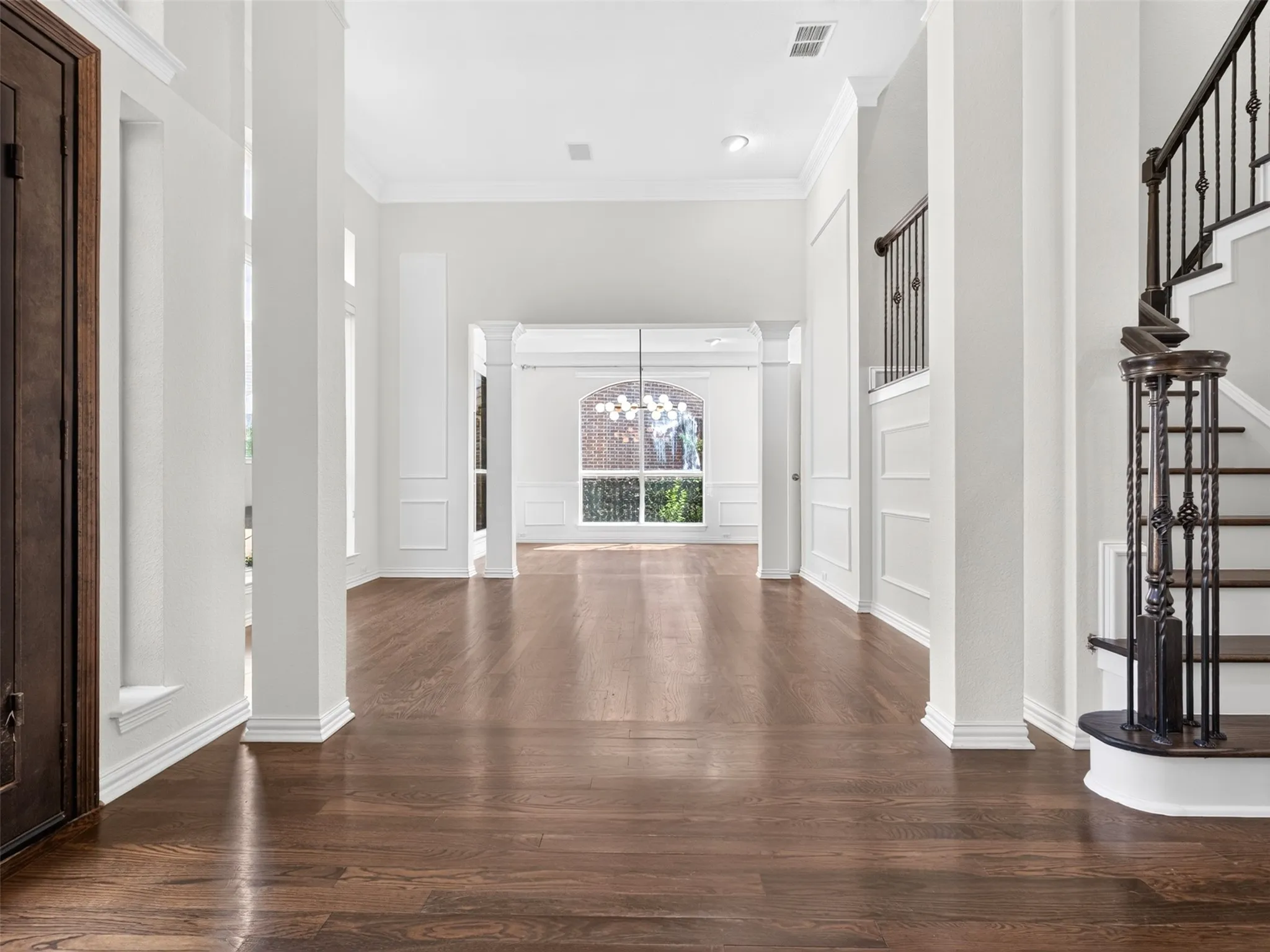 Hardwood flooring throughout, architectural columns, crown molding, wainscoting, and a grand staircase with wrought iron balusters