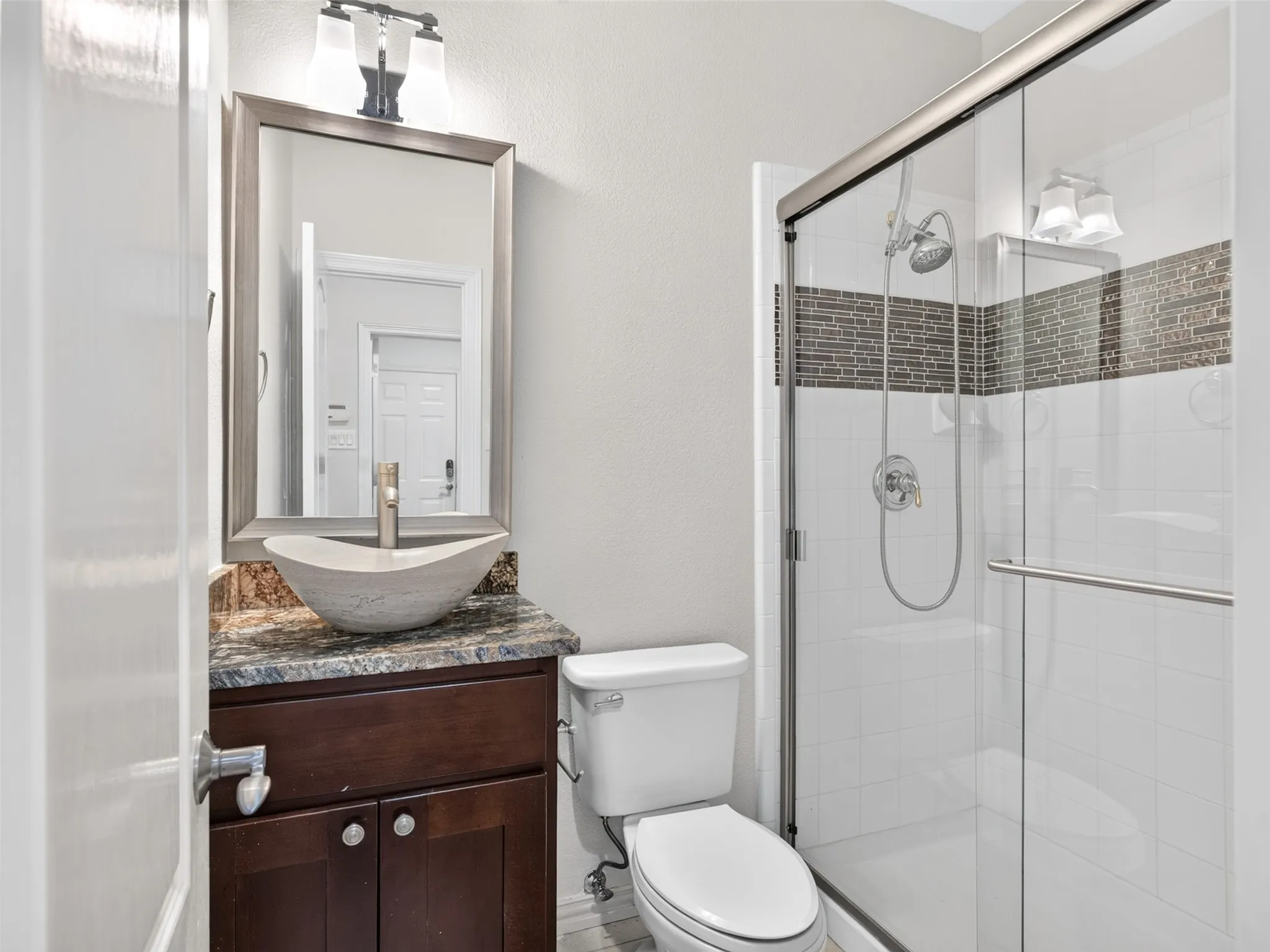 Vessel sink vanity with a stone countertop, framed mirror, and an enclosed shower with a mosaic tile accent