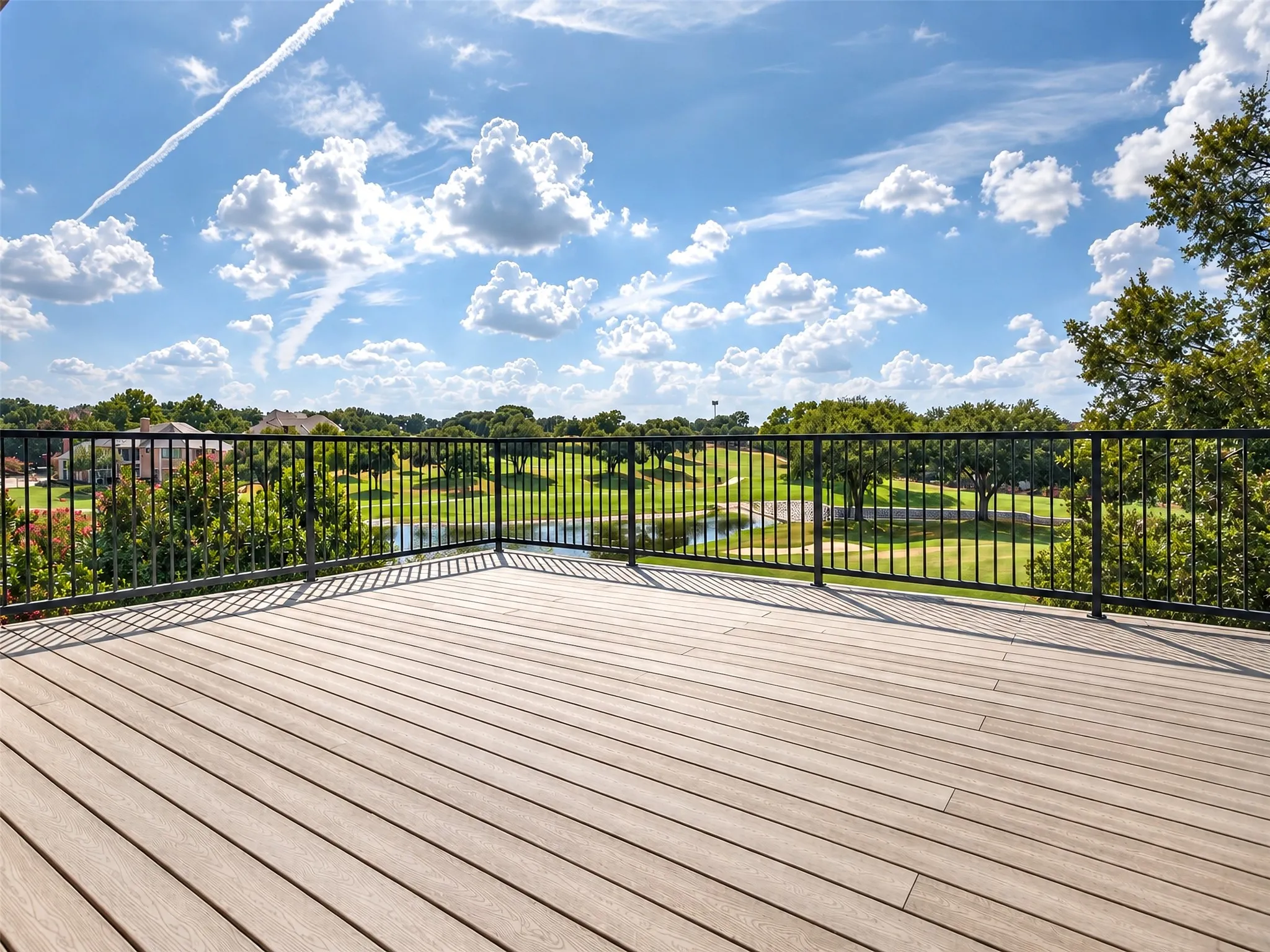 Expansive outdoor deck with composite decking and black metal railing, overlooking a golf course with a water feature and mature trees