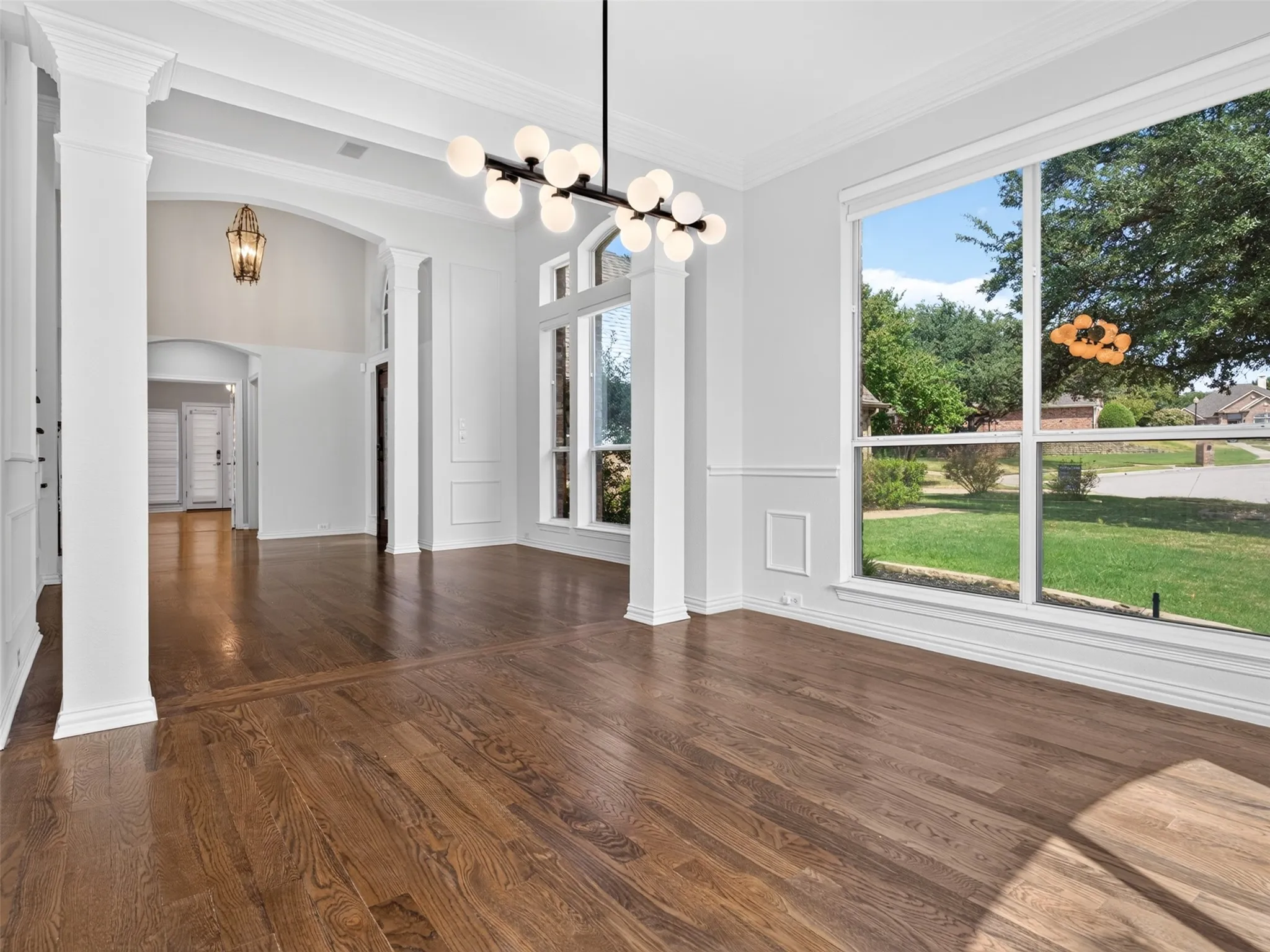 Spacious interior featuring wood-finish flooring, large picture windows, decorative wainscoting, and a contemporary chandelier