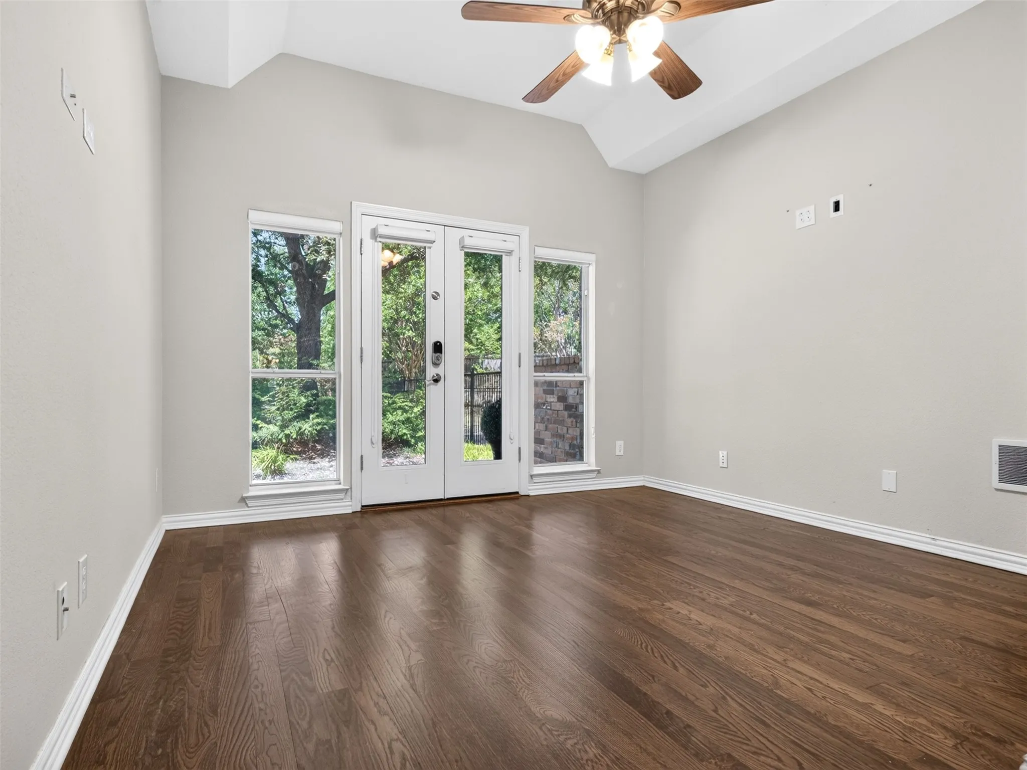 Vaulted ceiling, wood-finish flooring, white double French doors, dual windows, and ceiling fan with integrated lighting