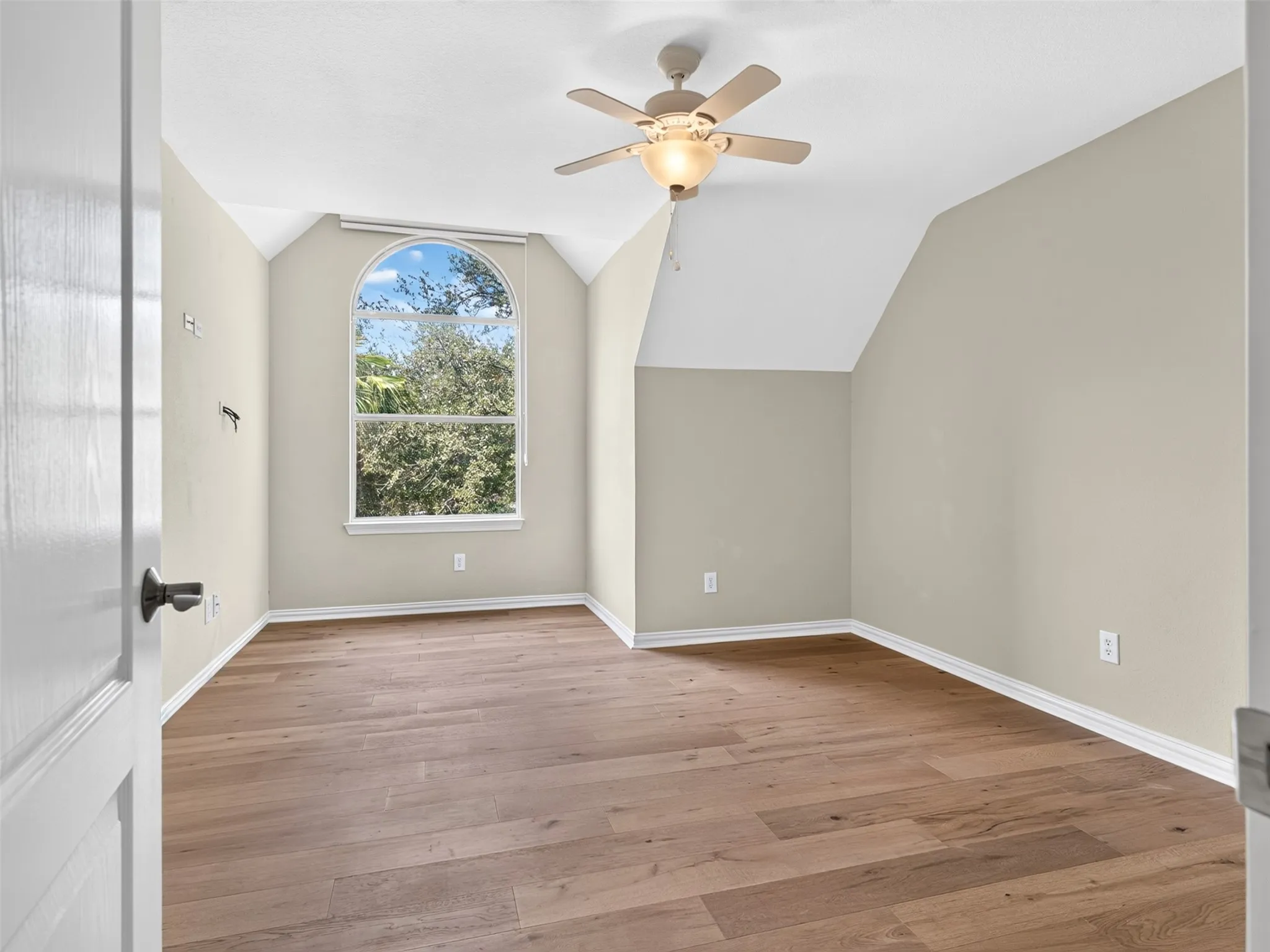 Wood-finish flooring, vaulted ceiling, arched window, and a ceiling fan with light fixture