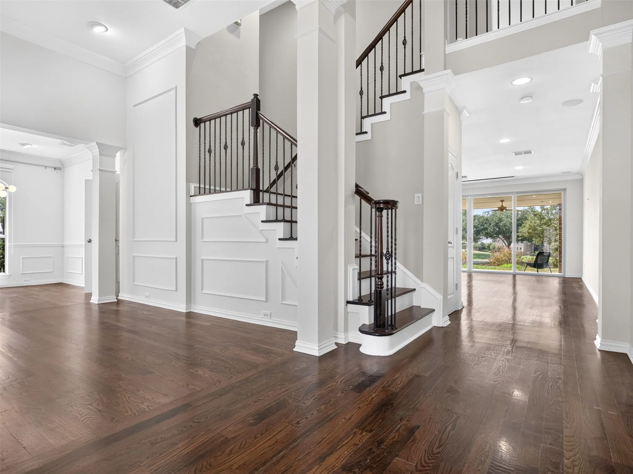 Two-story foyer with dark wood-finish flooring, a grand staircase with wrought iron balusters, extensive wall molding, and recessed lighting