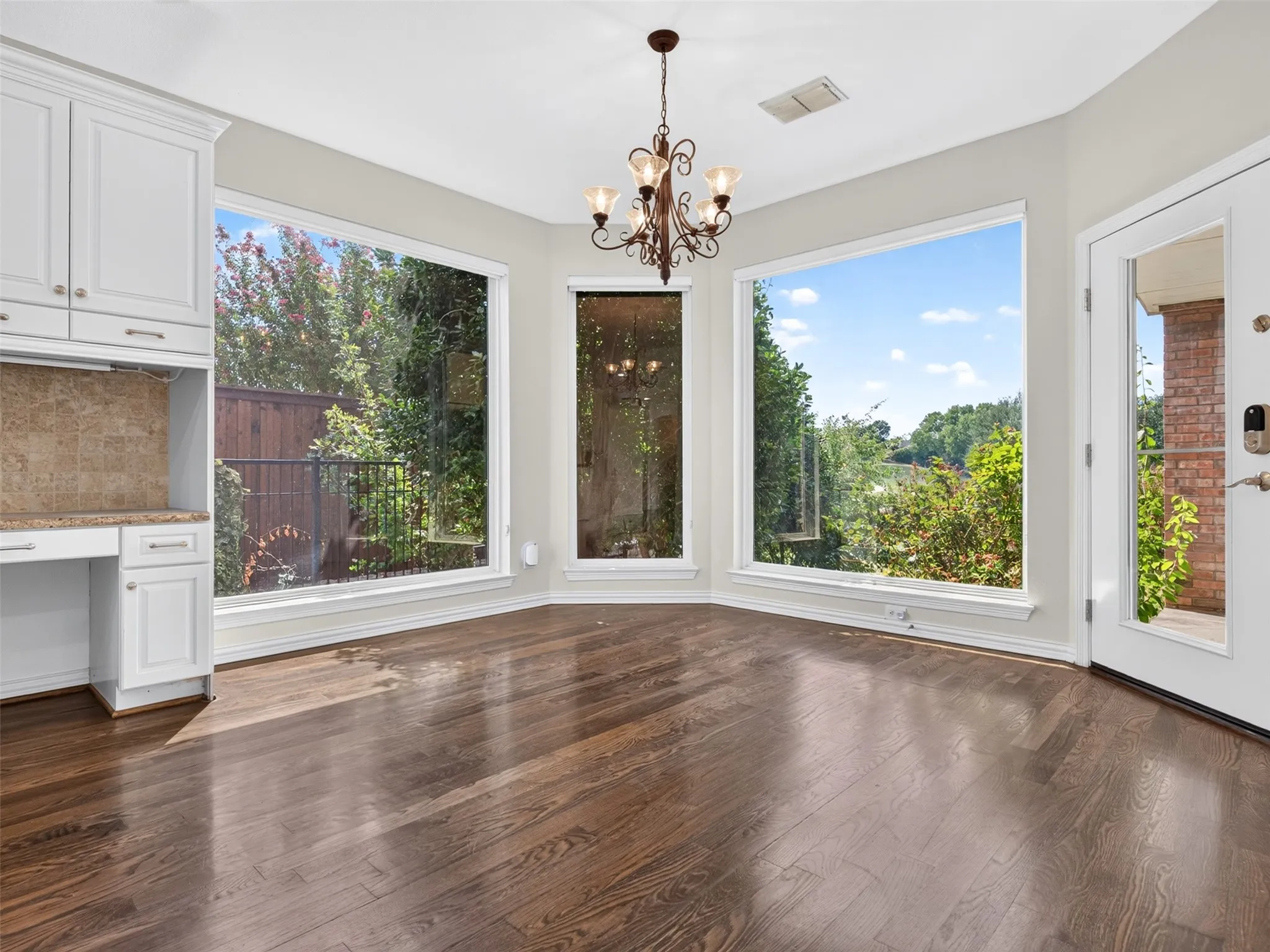 Hardwood flooring, built-in cabinetry, chandelier lighting, stone tile backsplash, and a glass-paneled door