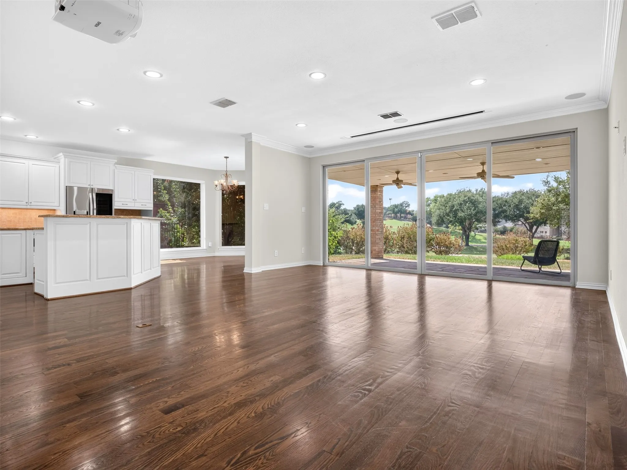 Expansive living area with wood-finish flooring, recessed lighting, and a projector