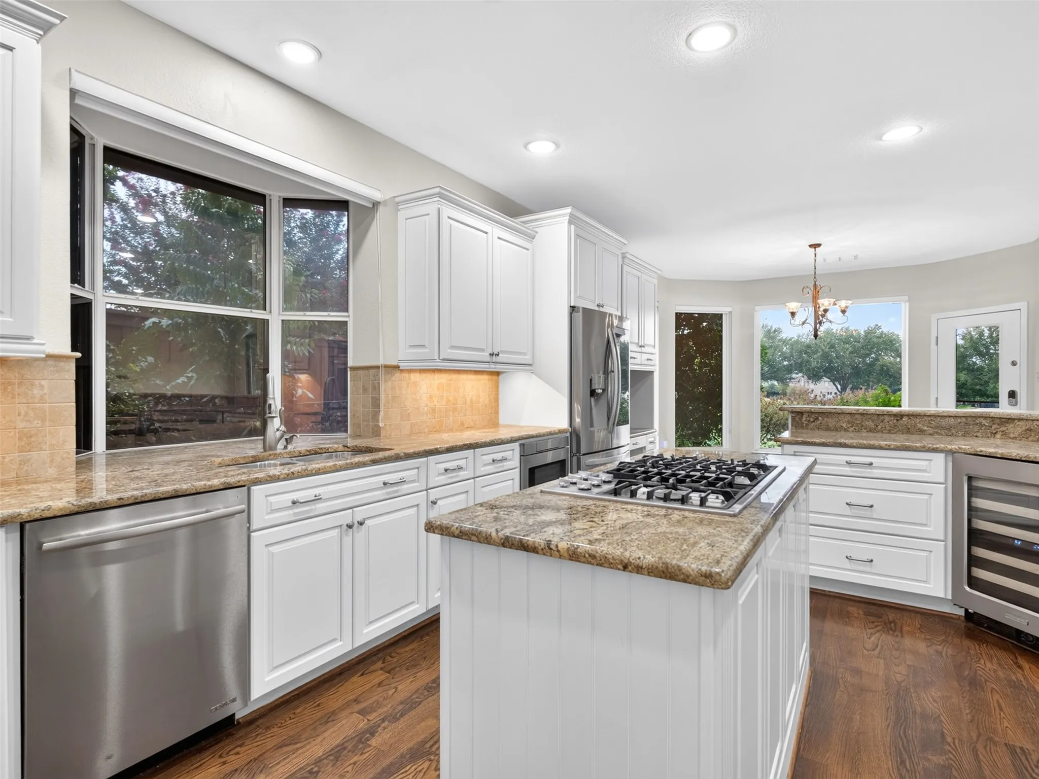 Kitchen featuring white cabinetry, stainless steel appliances, a gas cooktop on an island, granite countertops, and wood-finish flooring