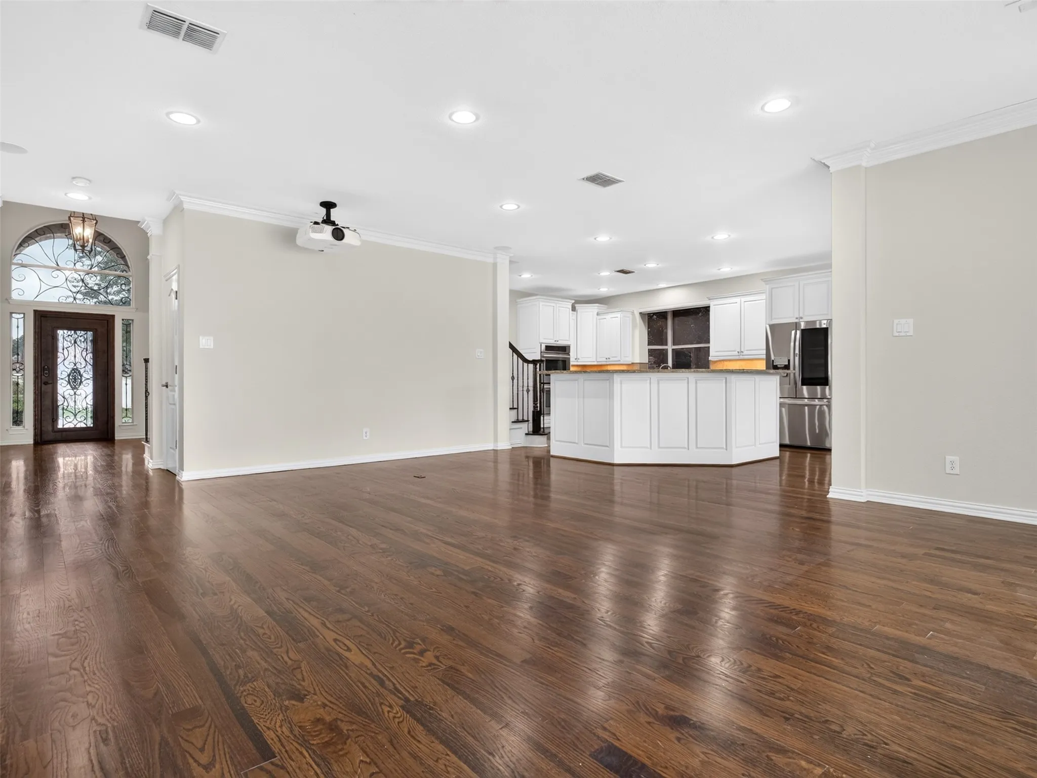 Wood-finish flooring throughout, recessed ceiling lighting, a decorative glass-paneled entry door with an arched transom, white kitchen cabinetry, and stainless steel appliances