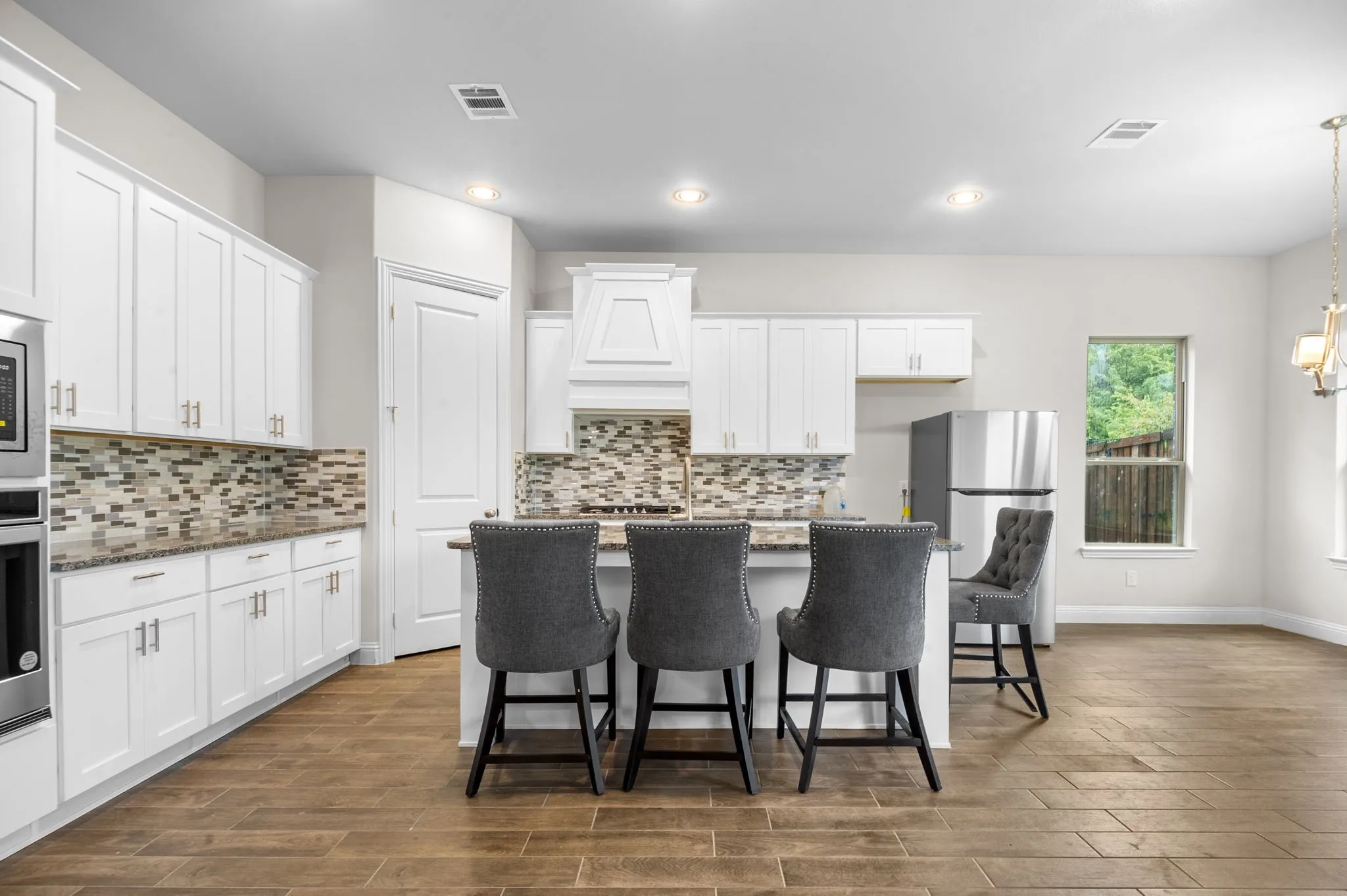 Kitchen with white cabinets, stainless steel appliances, dark hardwood / wood-style floors, dark stone counters, and a center island with sink