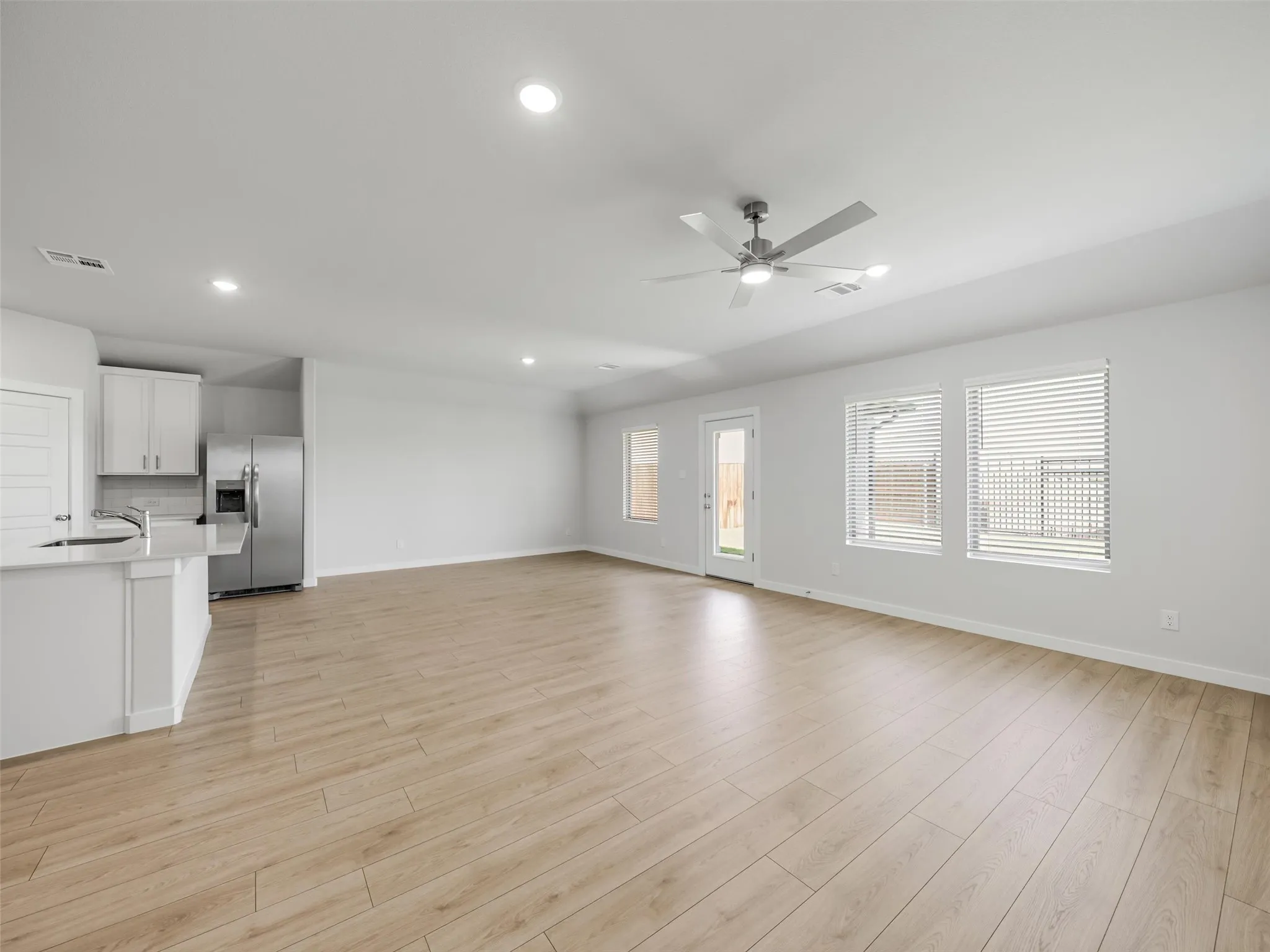 Expansive open-concept living area featuring light wood-finish flooring, recessed lighting, and a modern ceiling fan