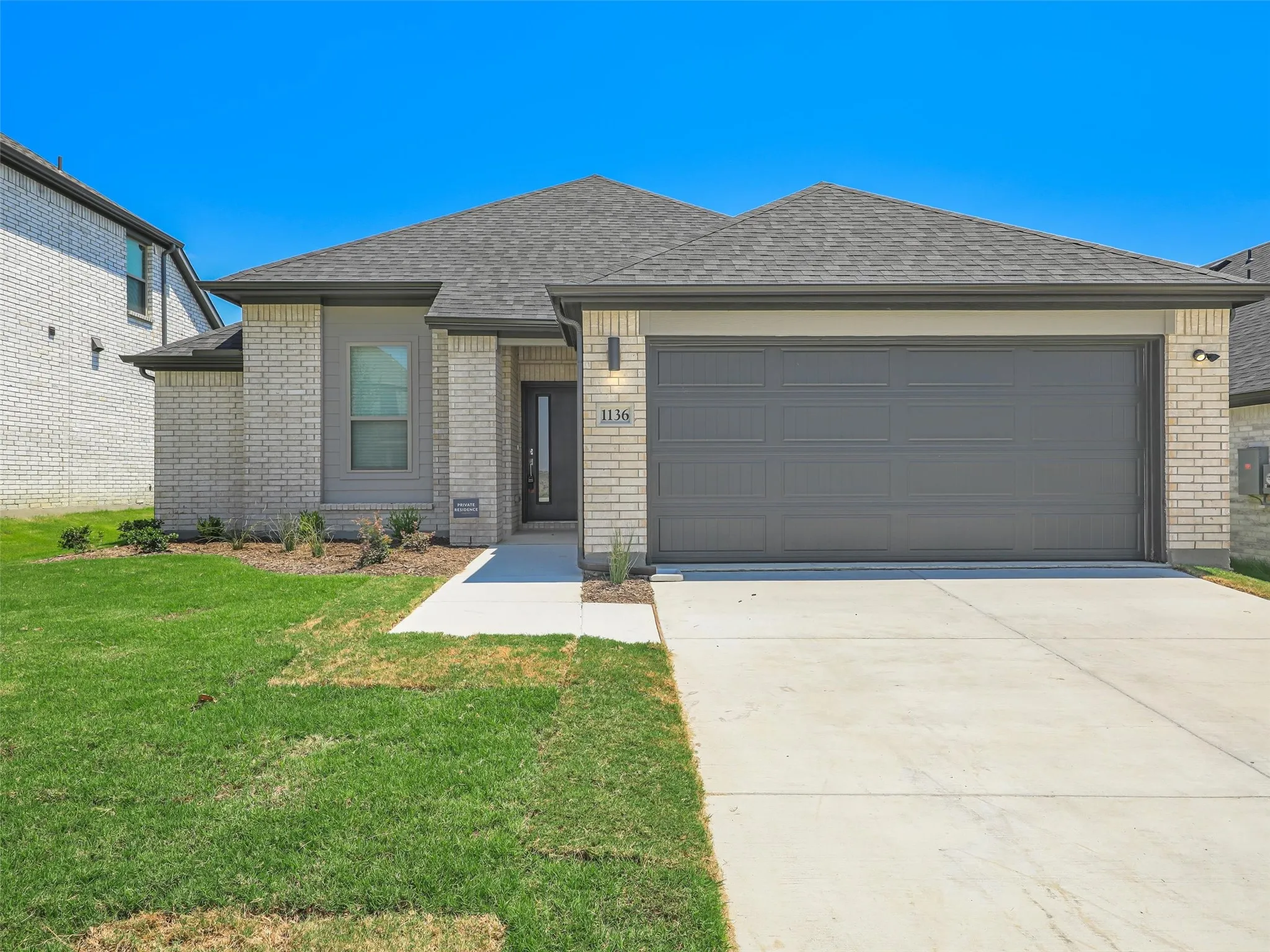 Welcoming brick home featuring a spacious two-car garage with contemporary gray paneling, a wide concrete driveway, and manicured front lawn
