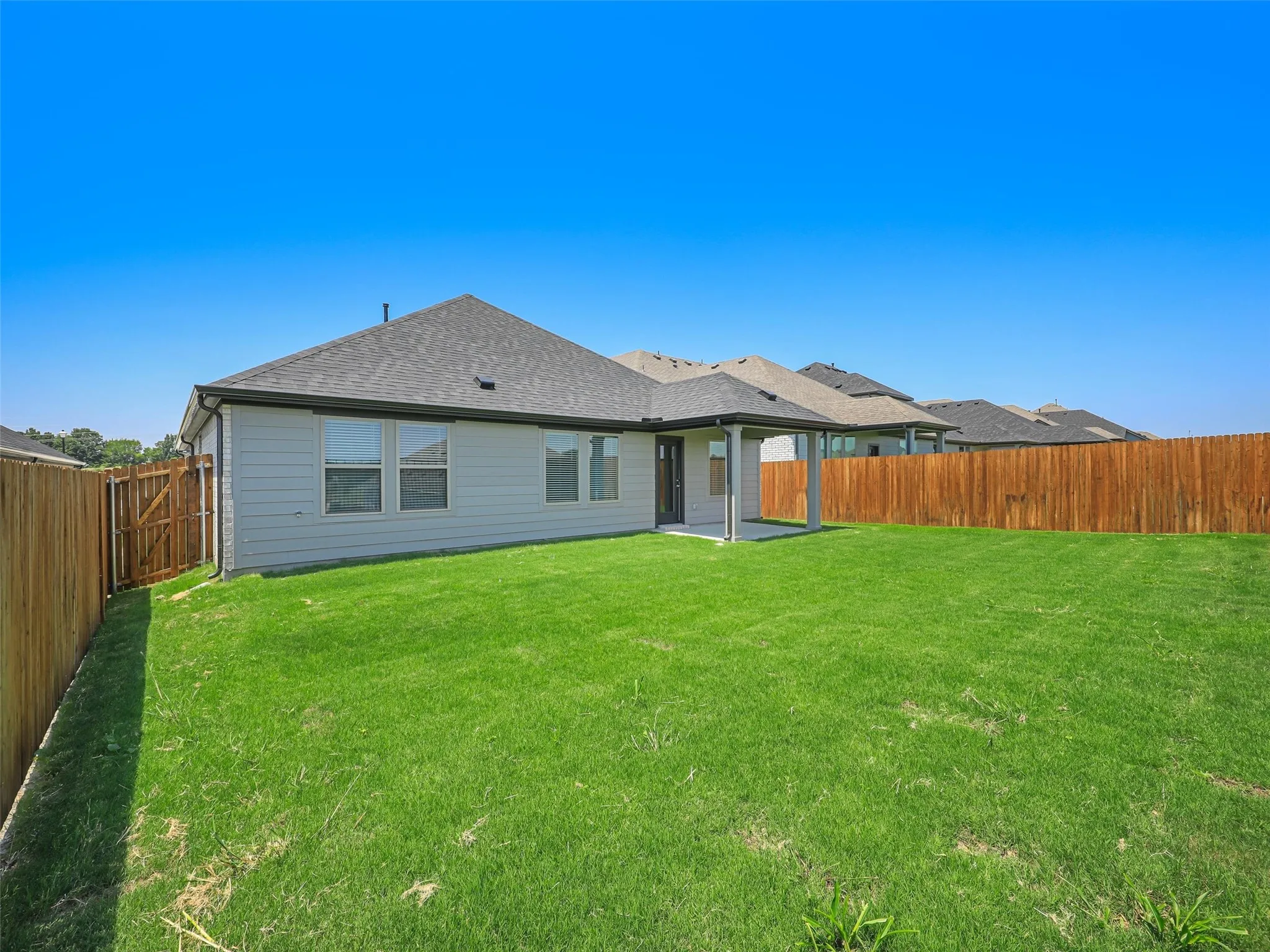 Expansive green lawn surrounds a single-story residence with light gray siding and a covered patio