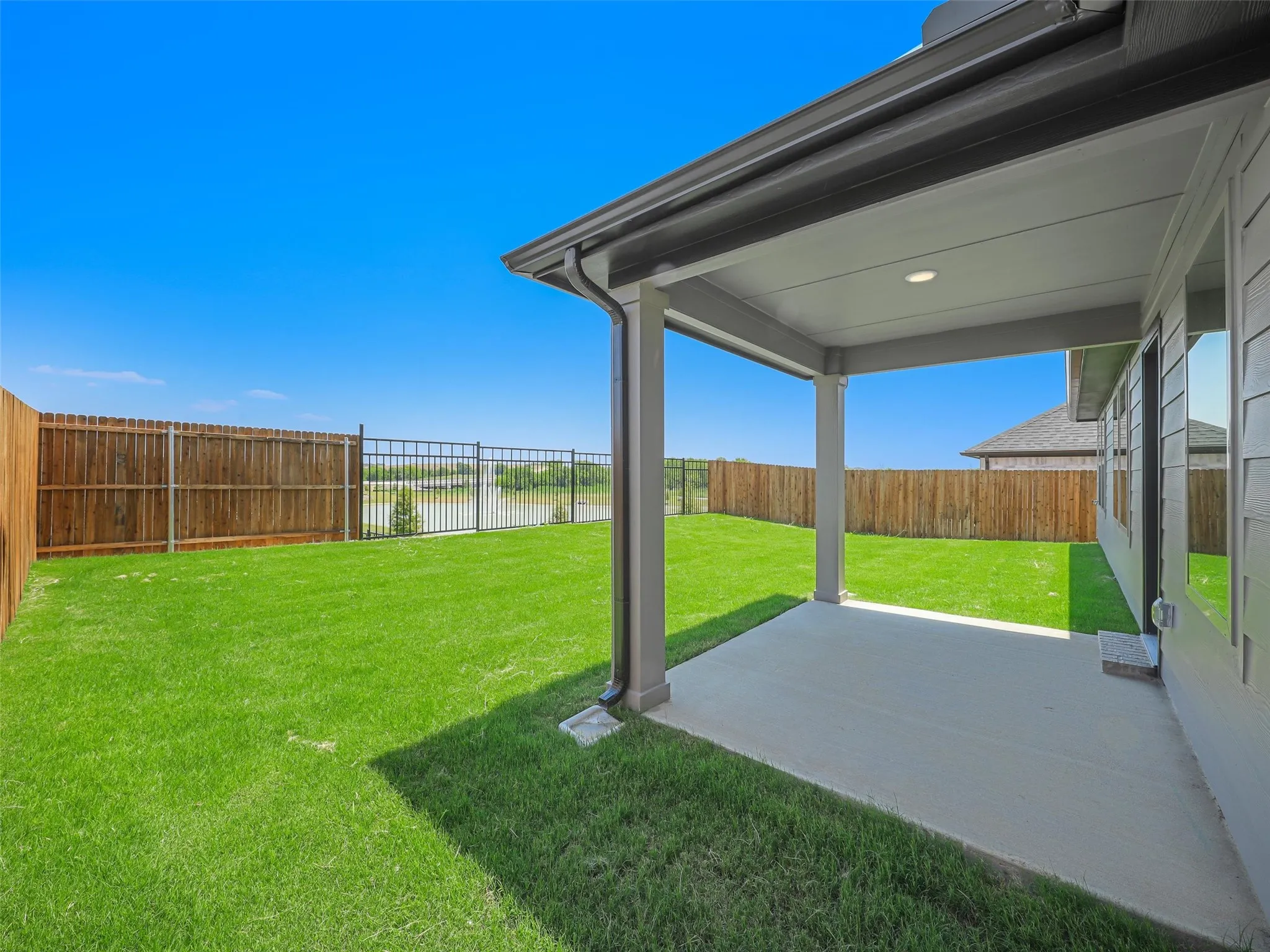Expansive backyard featuring a pristine manicured lawn, covered patio with recessed lighting, and wooden privacy fencing