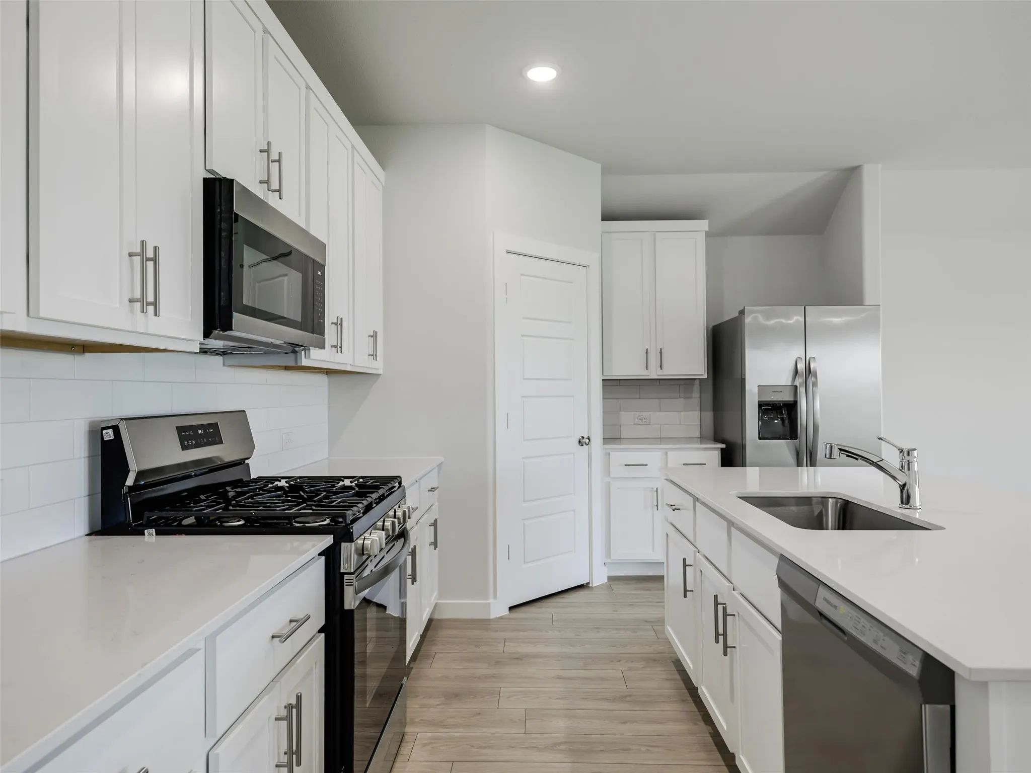 Modern kitchen featuring white cabinetry, light countertops, stainless steel appliances, a subway tile backsplash, and wood-finish flooring