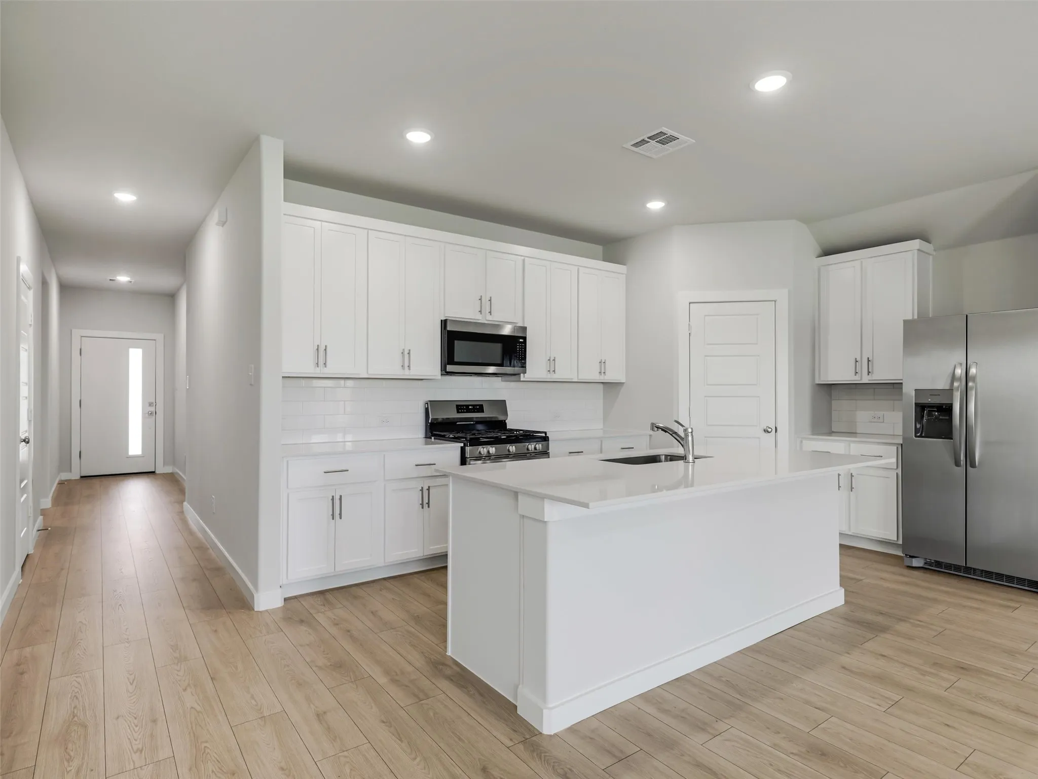 Kitchen featuring white shaker cabinetry, stainless steel appliances, a white subway tile backsplash, and a central island with a sink