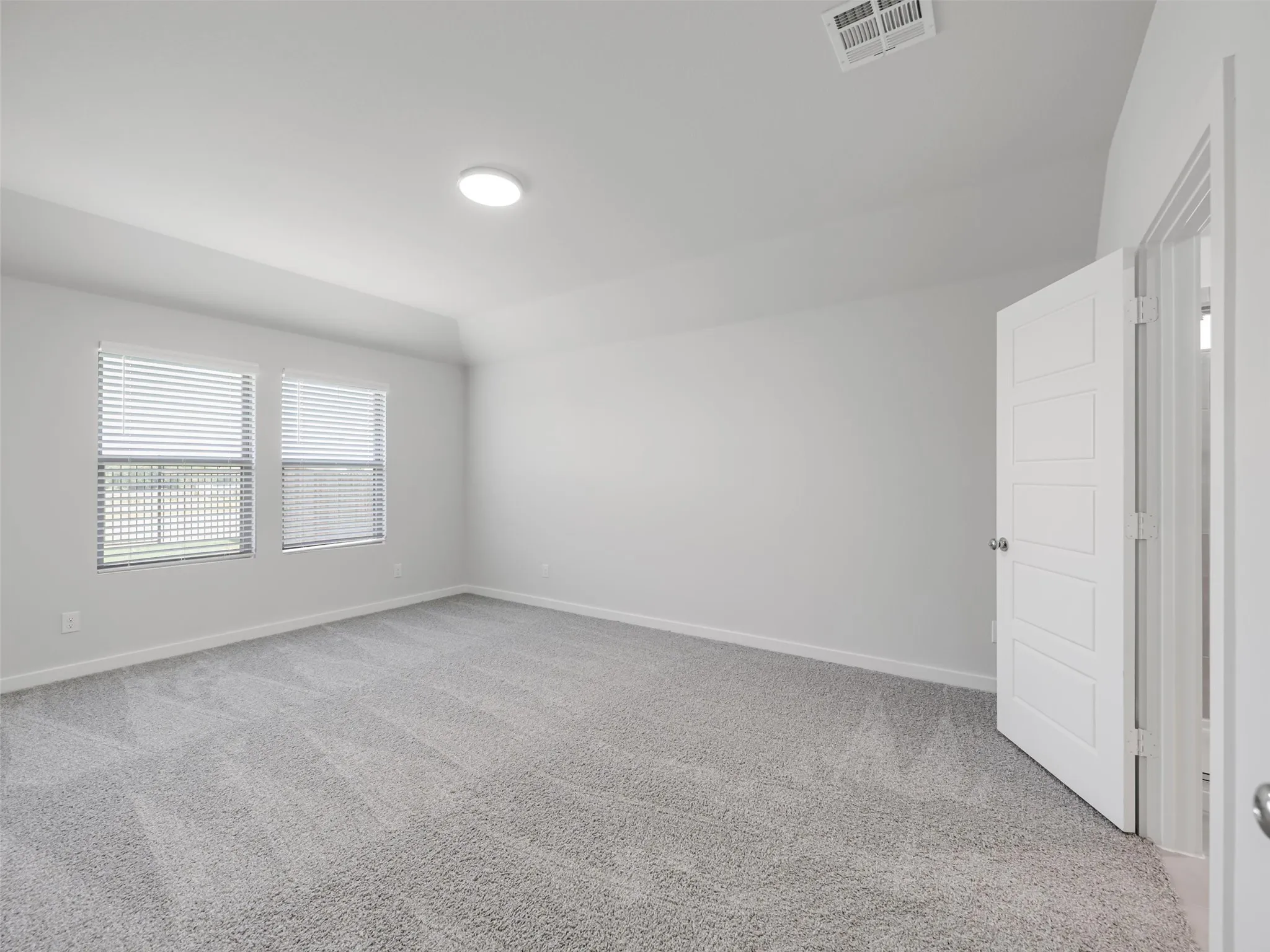 Bright and spacious bedroom featuring neutral carpeting, recessed ceiling lighting, dual windows with plantation shutters providing natural light, and a large reach-in closet with white panel doors