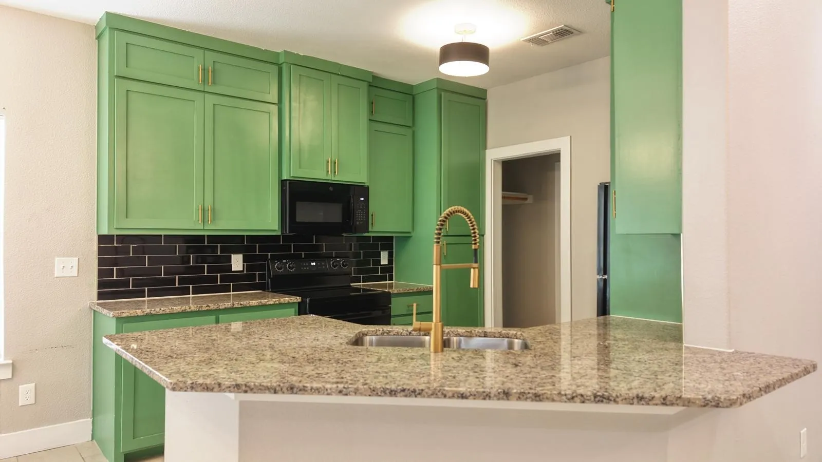Kitchen featuring green cabinetry, black subway tile backsplash, light-toned speckled countertops, and a gold-tone gooseneck faucet