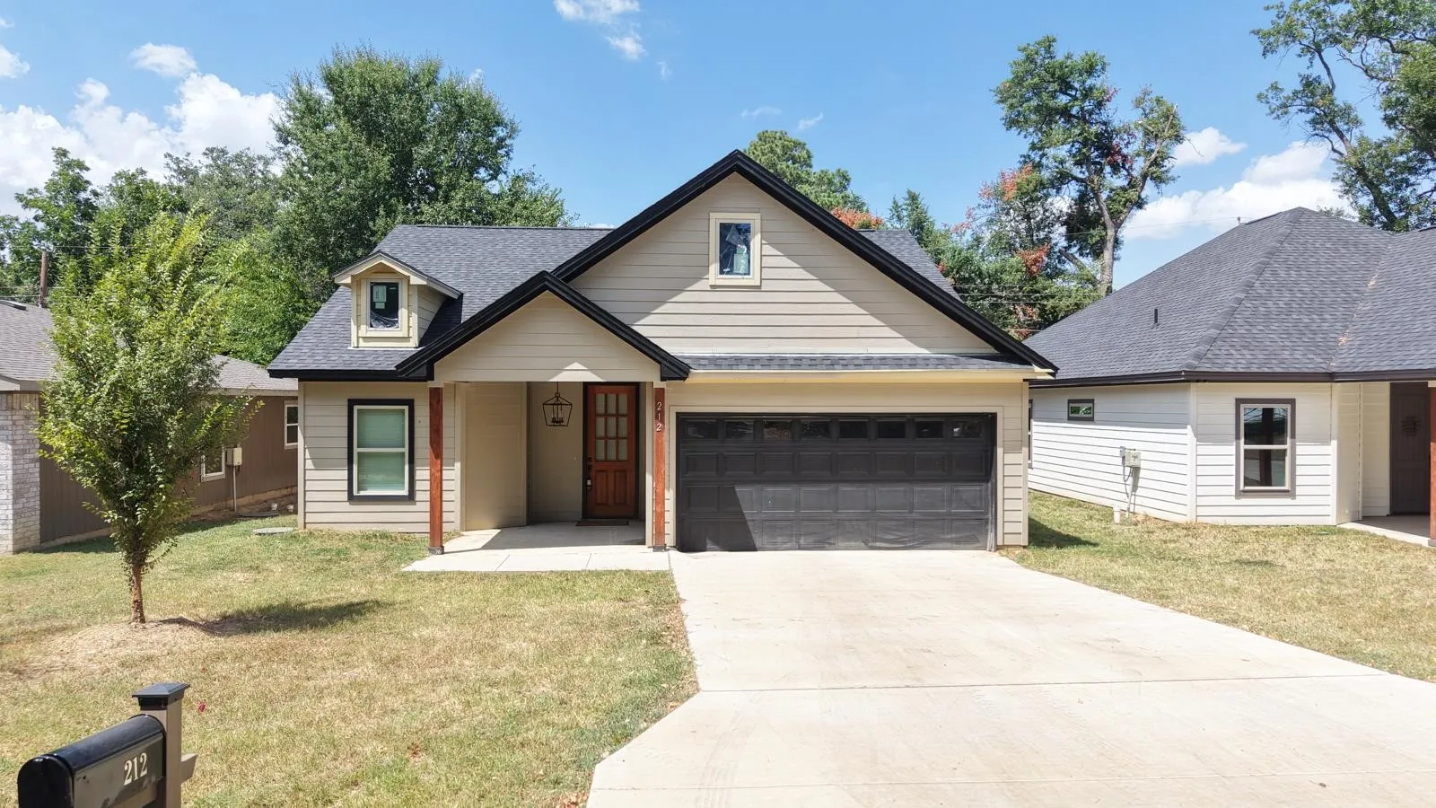 Single-story residence featuring light-colored siding, a dark roof, a two-car garage, a concrete driveway, and a covered entryway with a wooden front door
