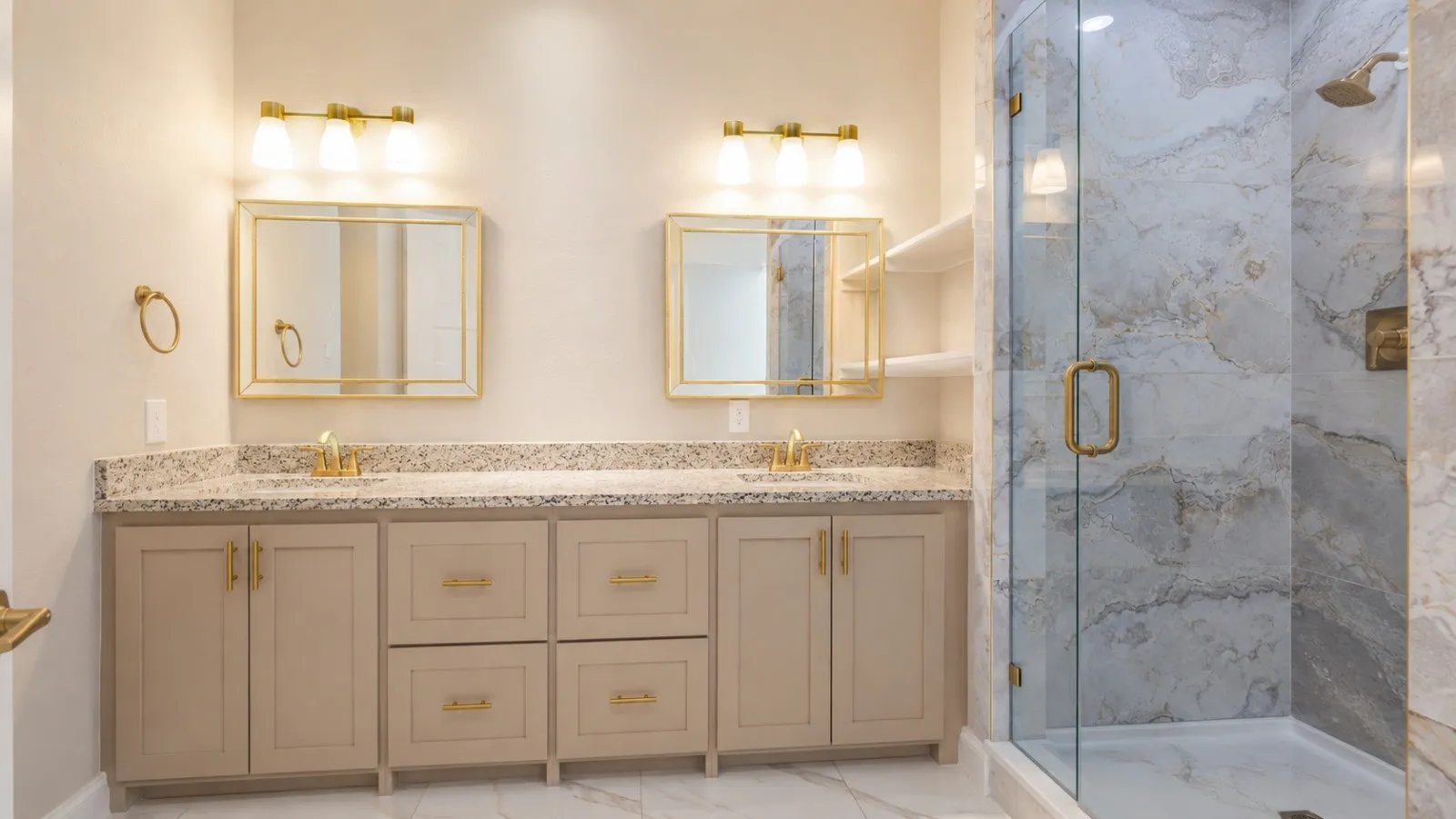 Dual vanity with granite countertops, gold-tone hardware, two framed mirrors, and a glass-enclosed shower with stone-look​​‌​​​​‌​​‌‌​‌‌​​​‌‌​‌​‌​‌​​​‌​​ tile