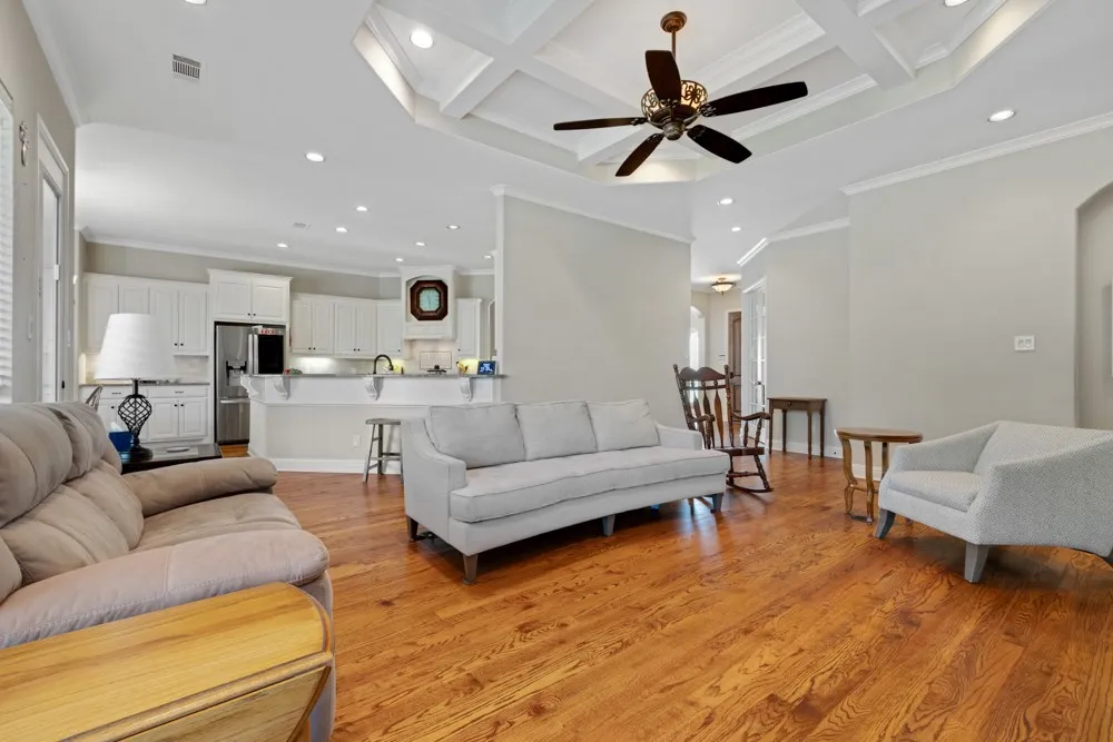 Open floor plan living area with coffered ceiling and open to the kitchen. Primary bedroom wing to the right.