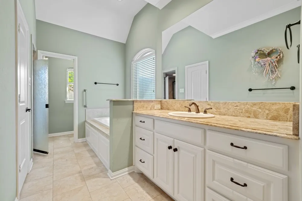 Primary bathroom features separate vanities and sinks, toilets on both sides, jetted tub and a walk-through shower with accessibility features such as handrails.