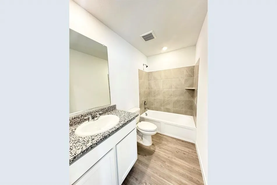 Full bathroom with tiled shower / bath combo, vanity, toilet, and wood-type flooring