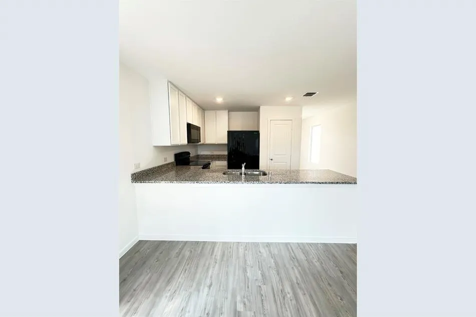 Kitchen with sink, stone countertops, white cabinetry, black appliances, and light hardwood / wood-style floors