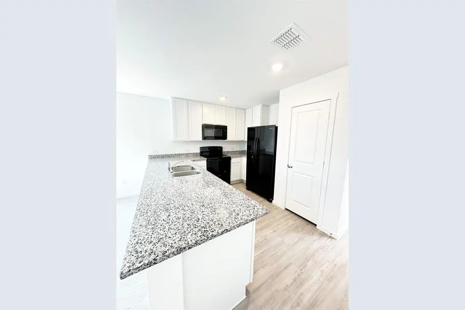 Kitchen with light wood-type flooring, kitchen peninsula, white cabinetry, black appliances, and light stone countertops