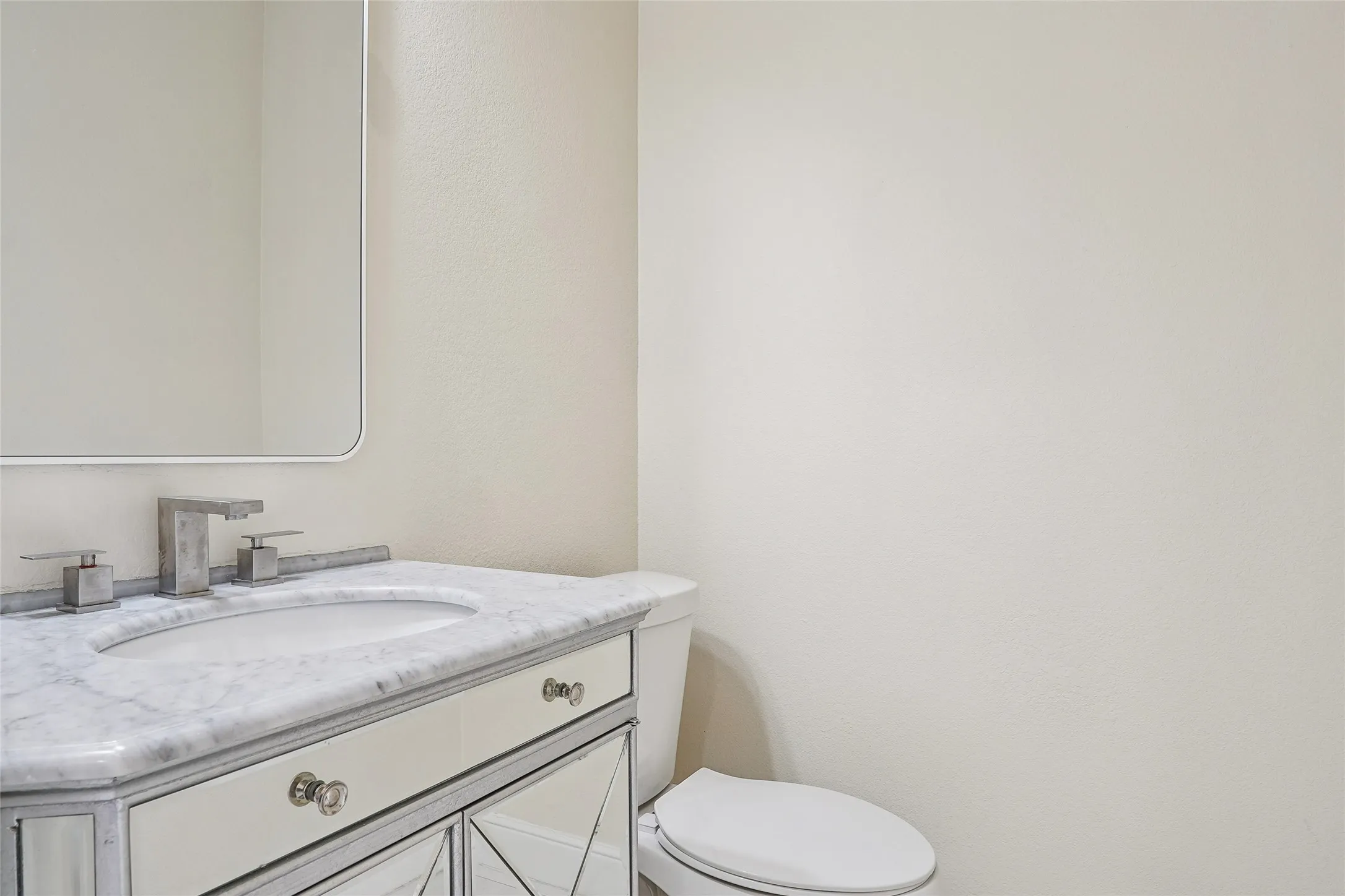Elegant bathroom vanity featuring a marble-top countertop, dual-handle chrome faucet, and custom cabinetry with decorative X-panel detailing
