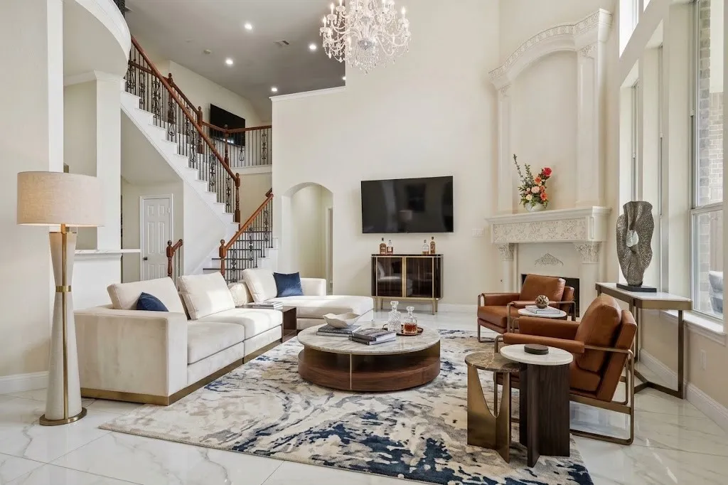 AI Staged, Vaulted ceilings with an ornate chandelier, a grand staircase with dark wood handrails and wrought iron balusters, a decorative fireplace with an intricately carved mantel, and large windows