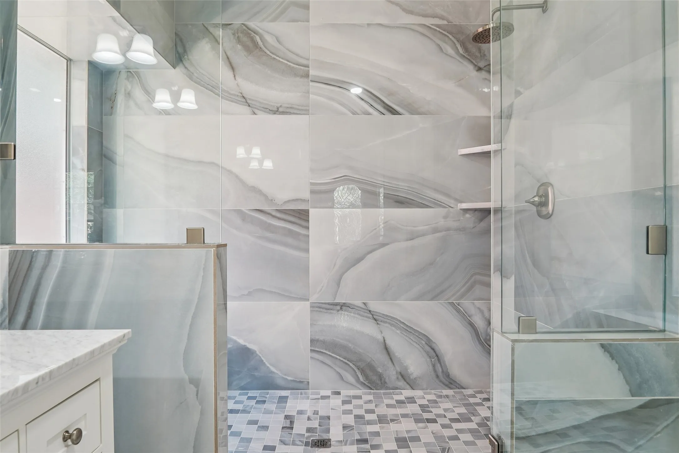 Walk-in shower with full glass enclosure and mosaic tile flooring