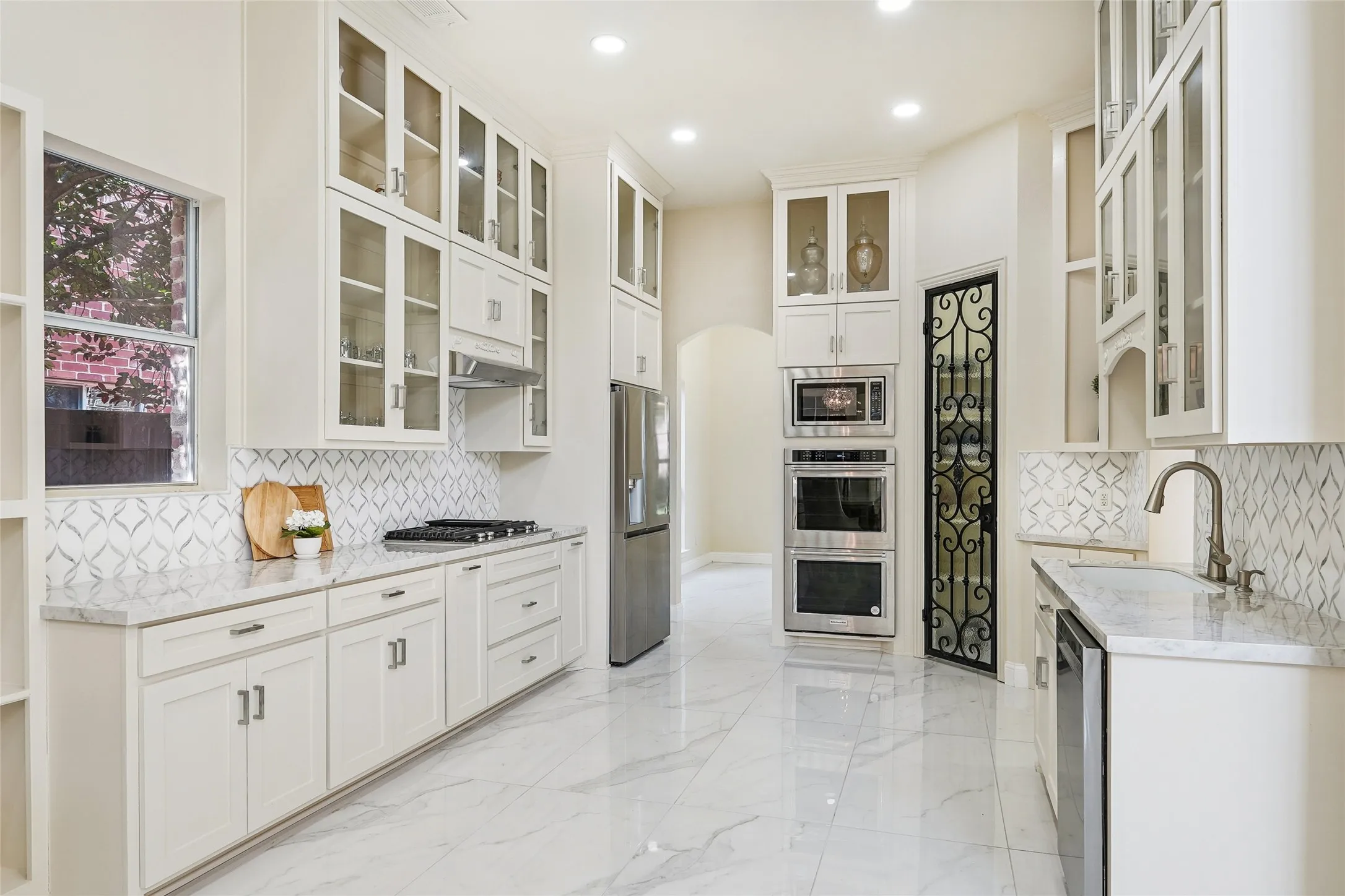 Spacious kitchen featuring extensive white cabinetry with glass-front uppers, stainless steel appliances, a gas cooktop, and an ornate iron-detail door
