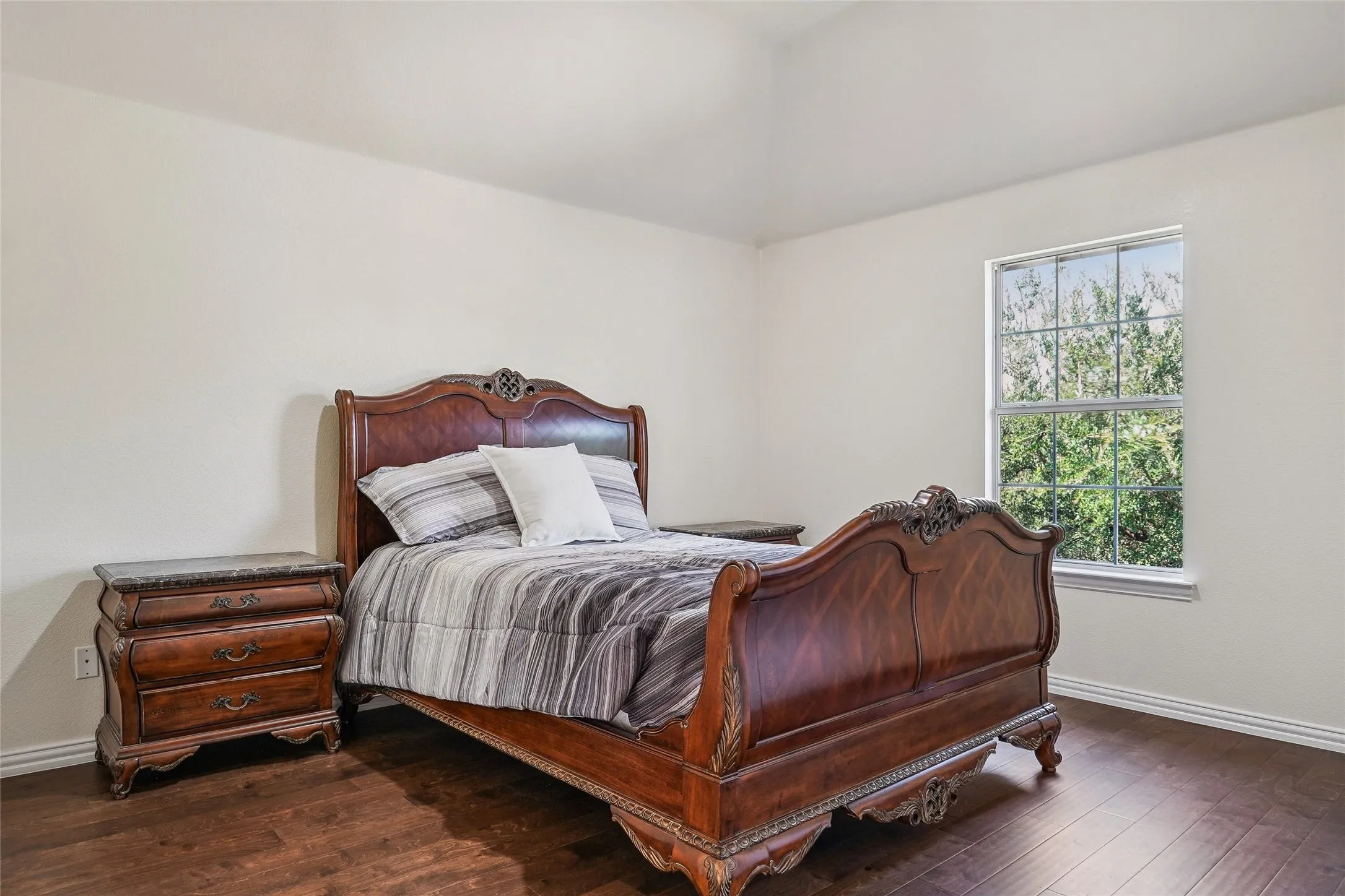 Vaulted ceiling bedroom featuring wood-finish flooring, a double-paned window, and white baseboards