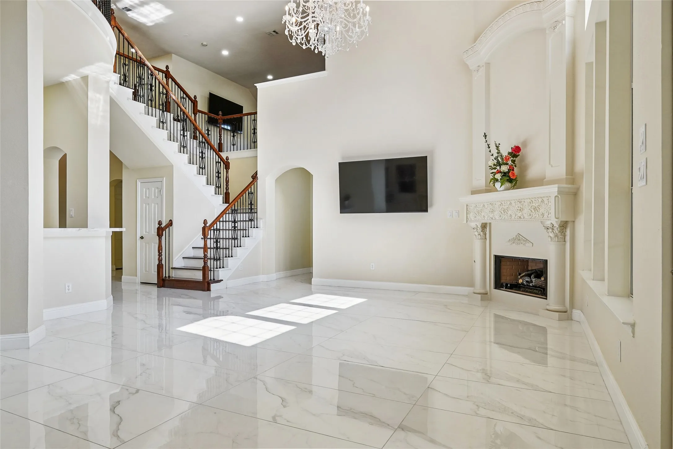 Grand entry featuring a two-story ceiling, a sweeping staircase with dark wood handrails and wrought iron balusters, and expansive marble-look tile flooring