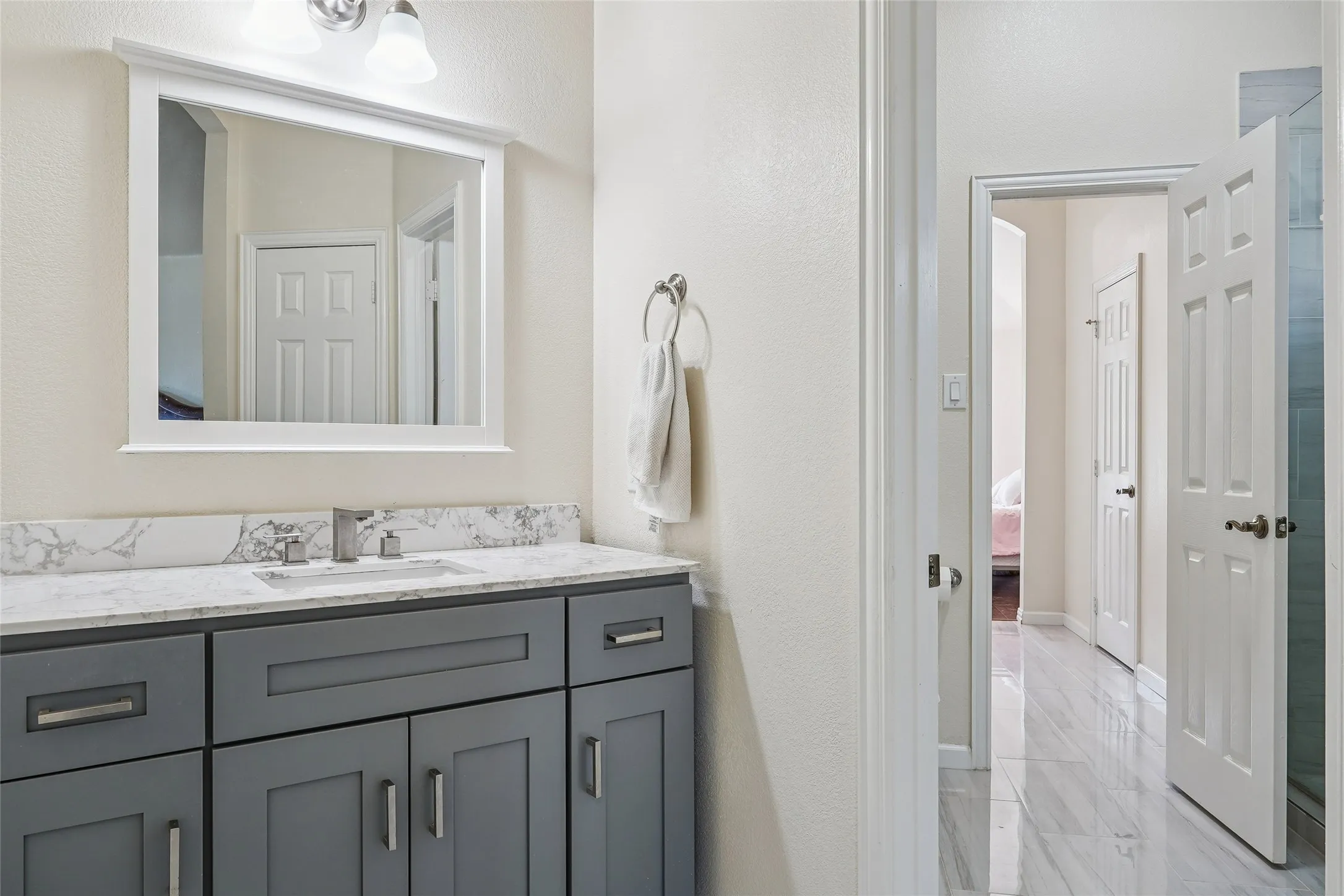 Bathroom vanity featuring a single basin sink, chrome faucet, and a light-colored countertop with a distinct veining pattern
