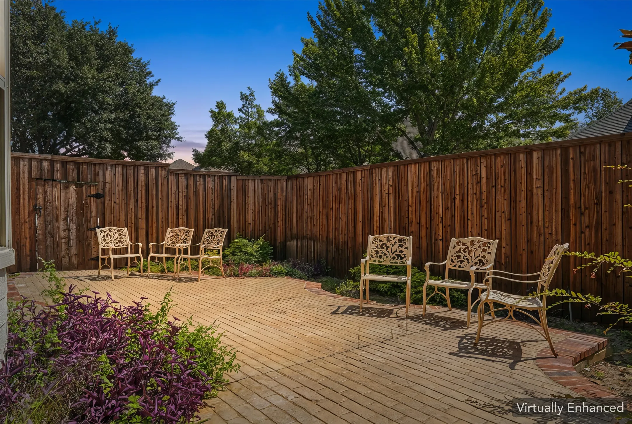 Private outdoor patio featuring a paver stone surface, perimeter wood fencing, and mature trees overhead