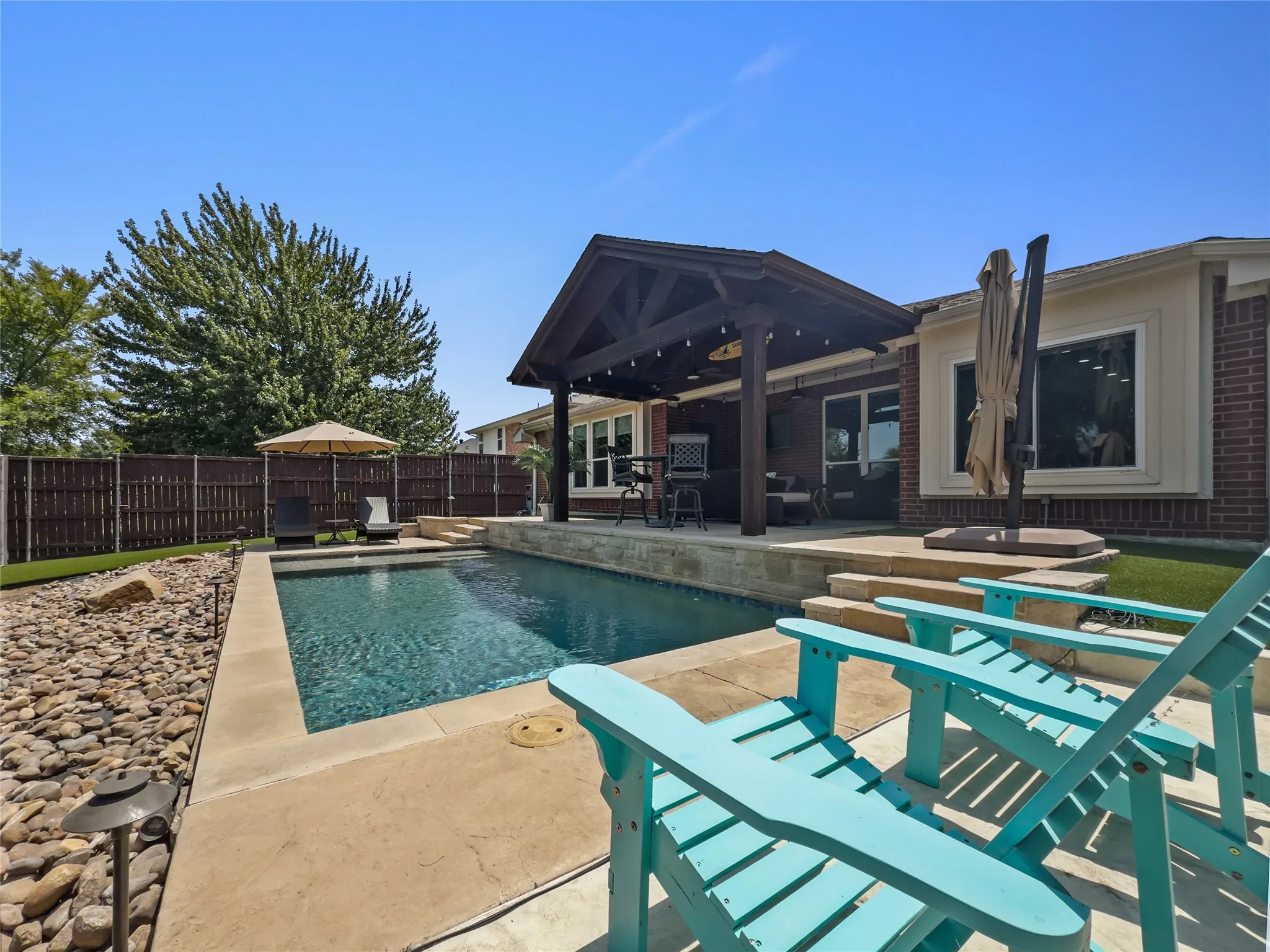 Private swimming pool with concrete decking, a dark wood pergola, and a brick exterior