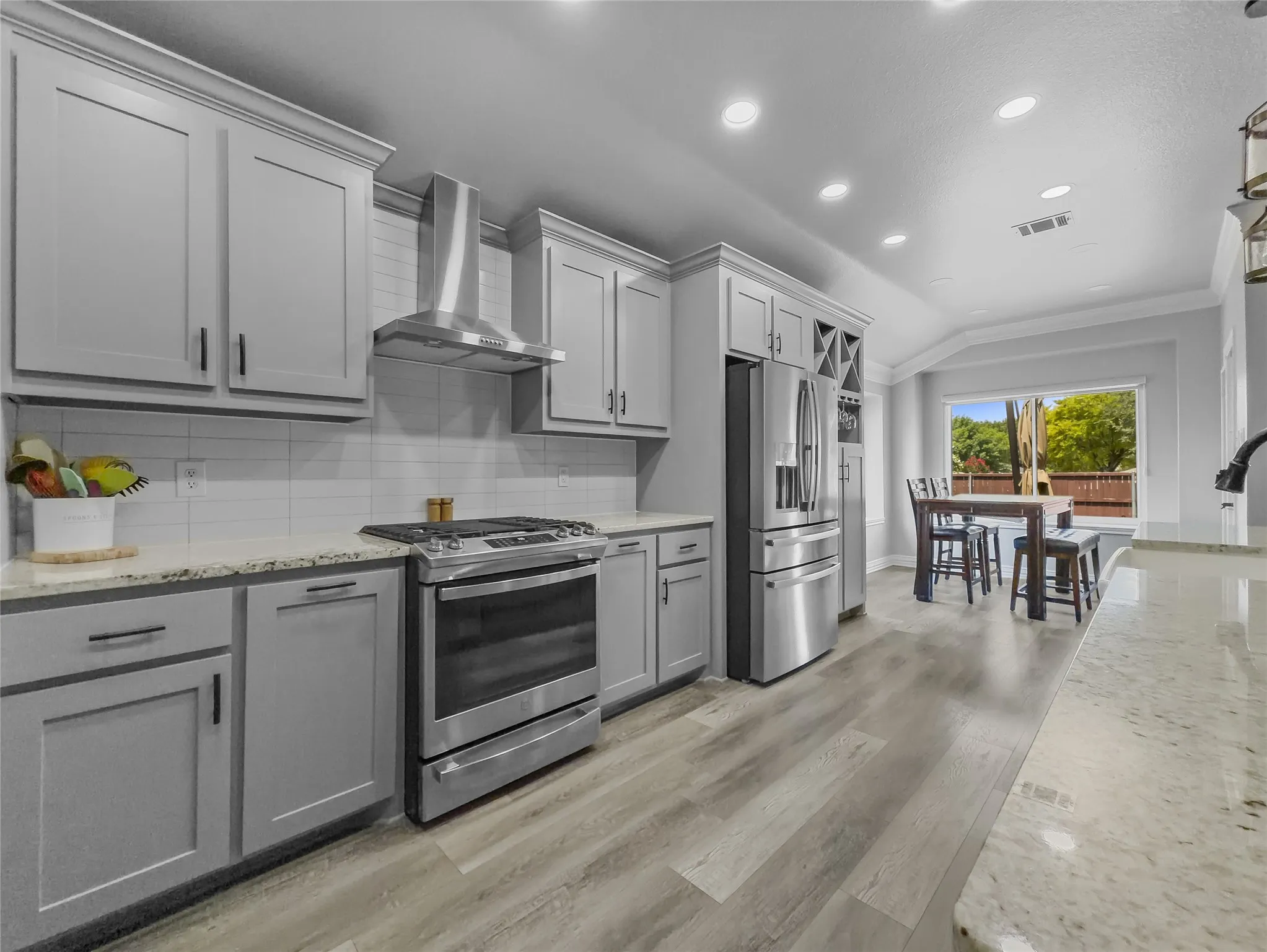 Light gray cabinetry with crown molding, stainless steel appliances, granite countertops, wood-finish flooring, and a white subway tile backsplash