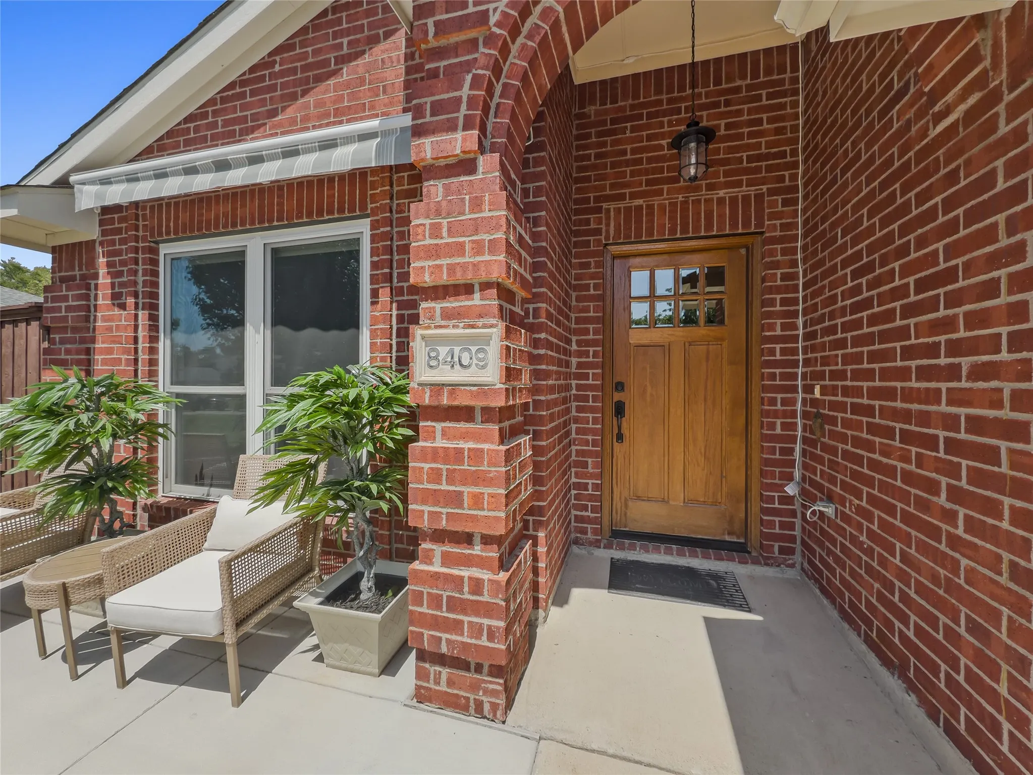 Brick exterior with an arched entryway, natural wood front door, and a striped window awning
