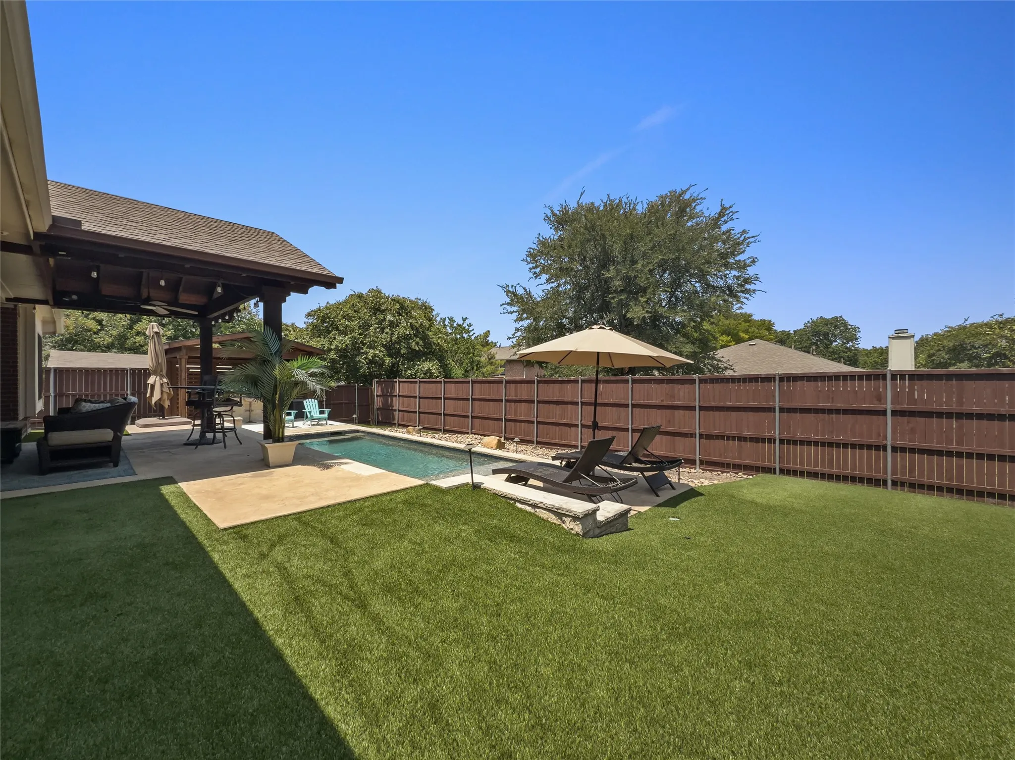 Expansive backyard featuring a covered patio, swimming pool, artificial turf, and wood privacy fencing