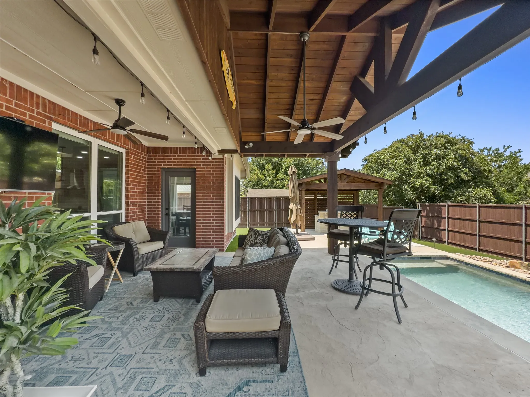 Expansive covered patio featuring a wood-beam ceiling, ceiling fans, and string lighting
