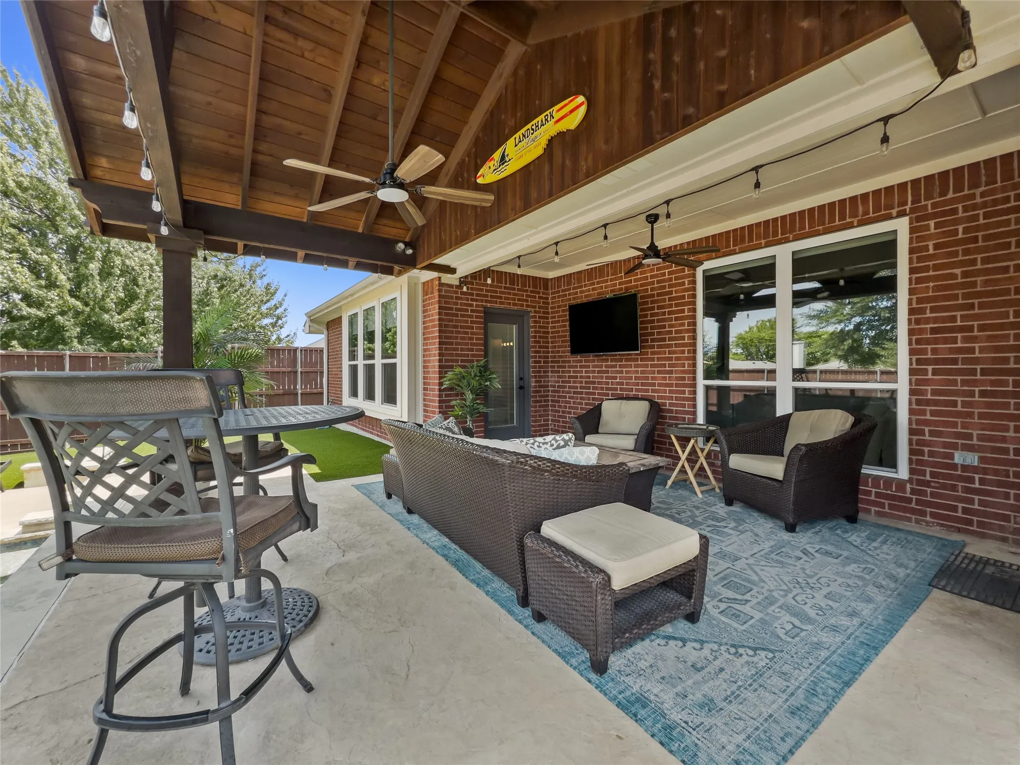 Expansive covered patio featuring a wood-panel ceiling, ceiling fans, string lighting, and a brick exterior