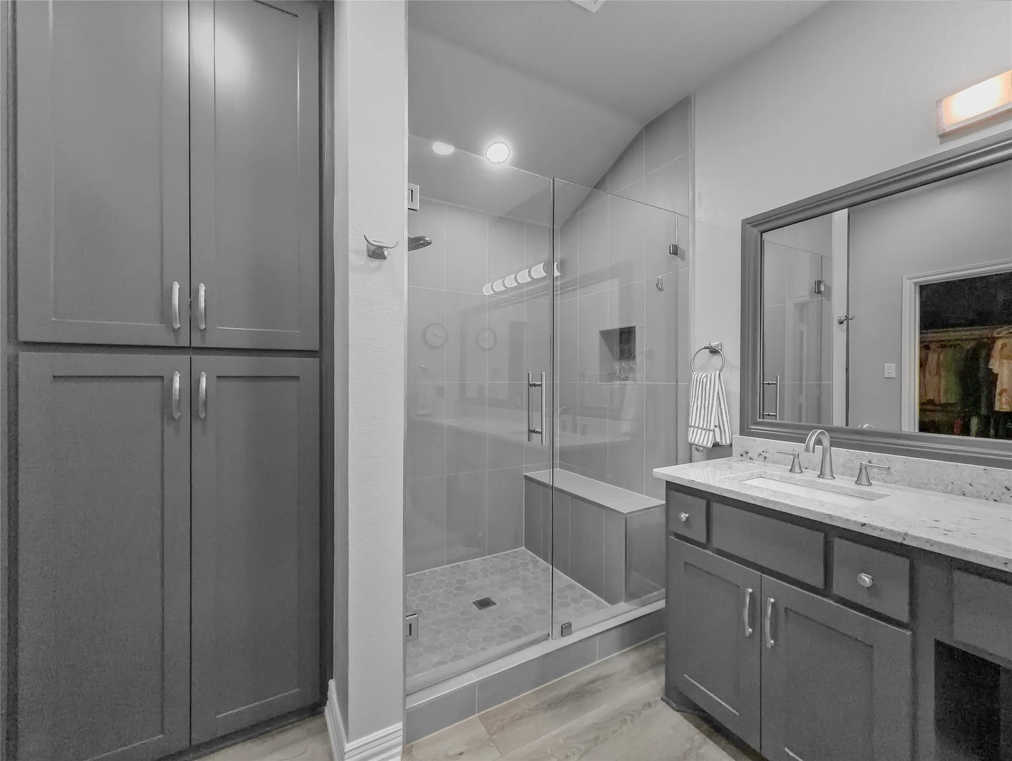 Spacious bathroom featuring a glass-enclosed shower with a built-in bench, dual vanity with a stone countertop, framed mirror, and extensive built-in cabinetry