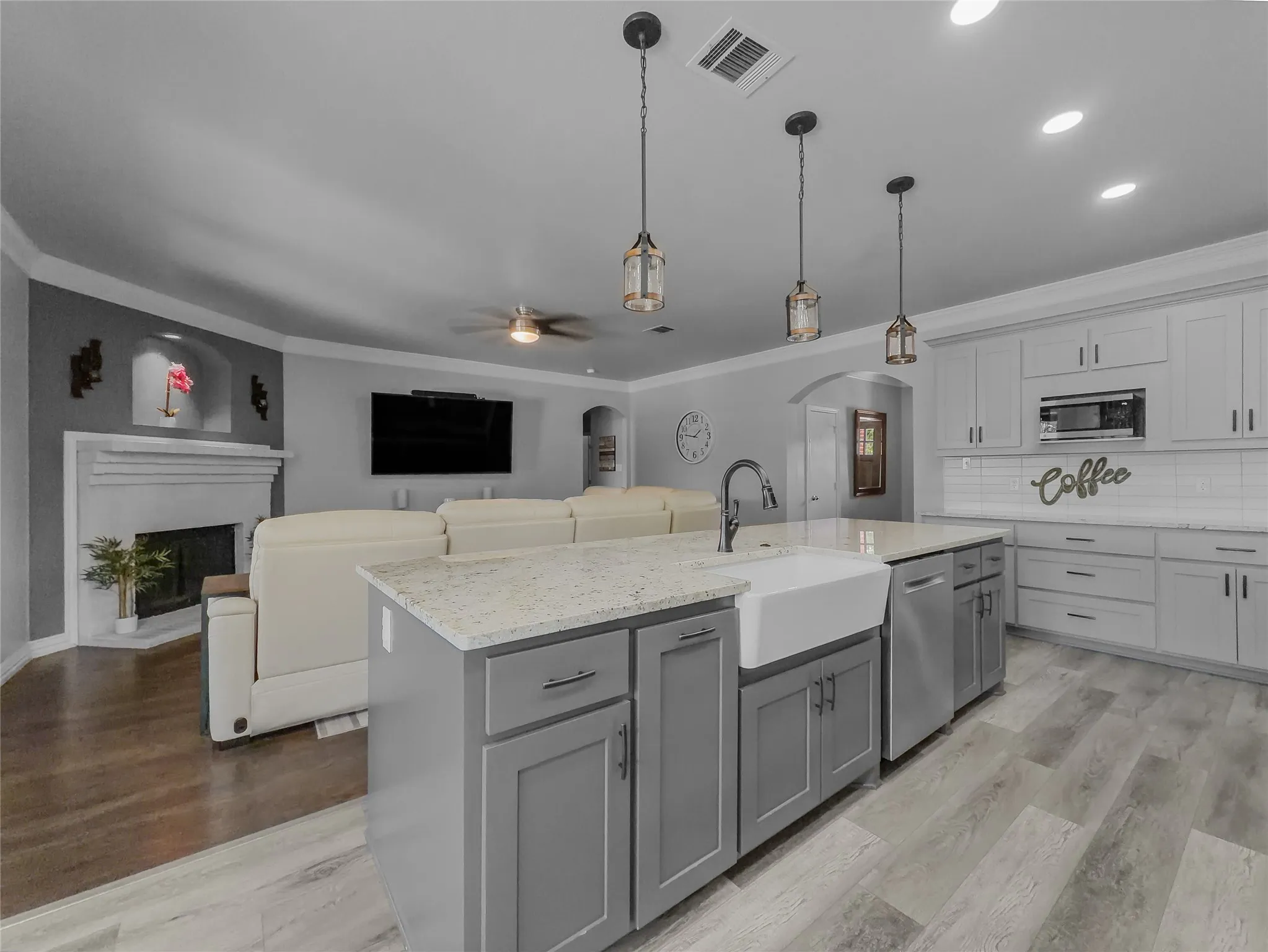 Open-concept living space with a kitchen island featuring a white farmhouse sink and integrated dishwasher