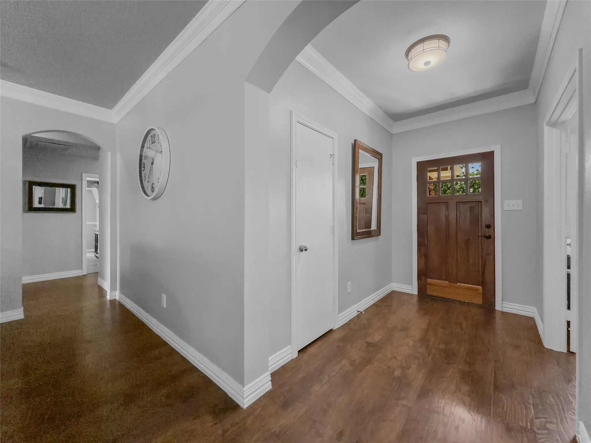 Entryway featuring wood-finish flooring, crown molding, a wood-paneled door with glass inserts, and an arched hallway