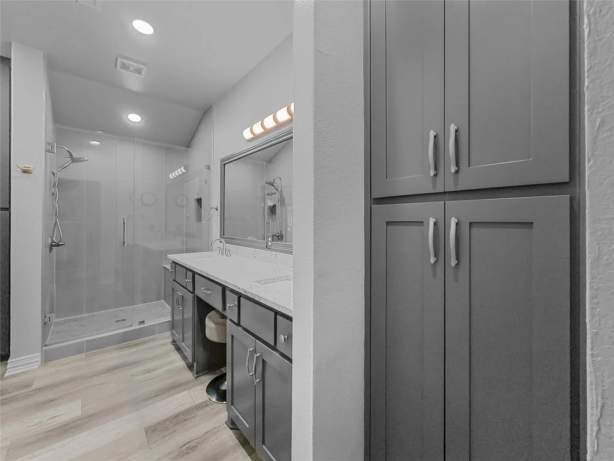 Dual vanity with integrated sinks, glass-enclosed shower, built-in storage cabinetry, wood-finish flooring, and recessed lighting