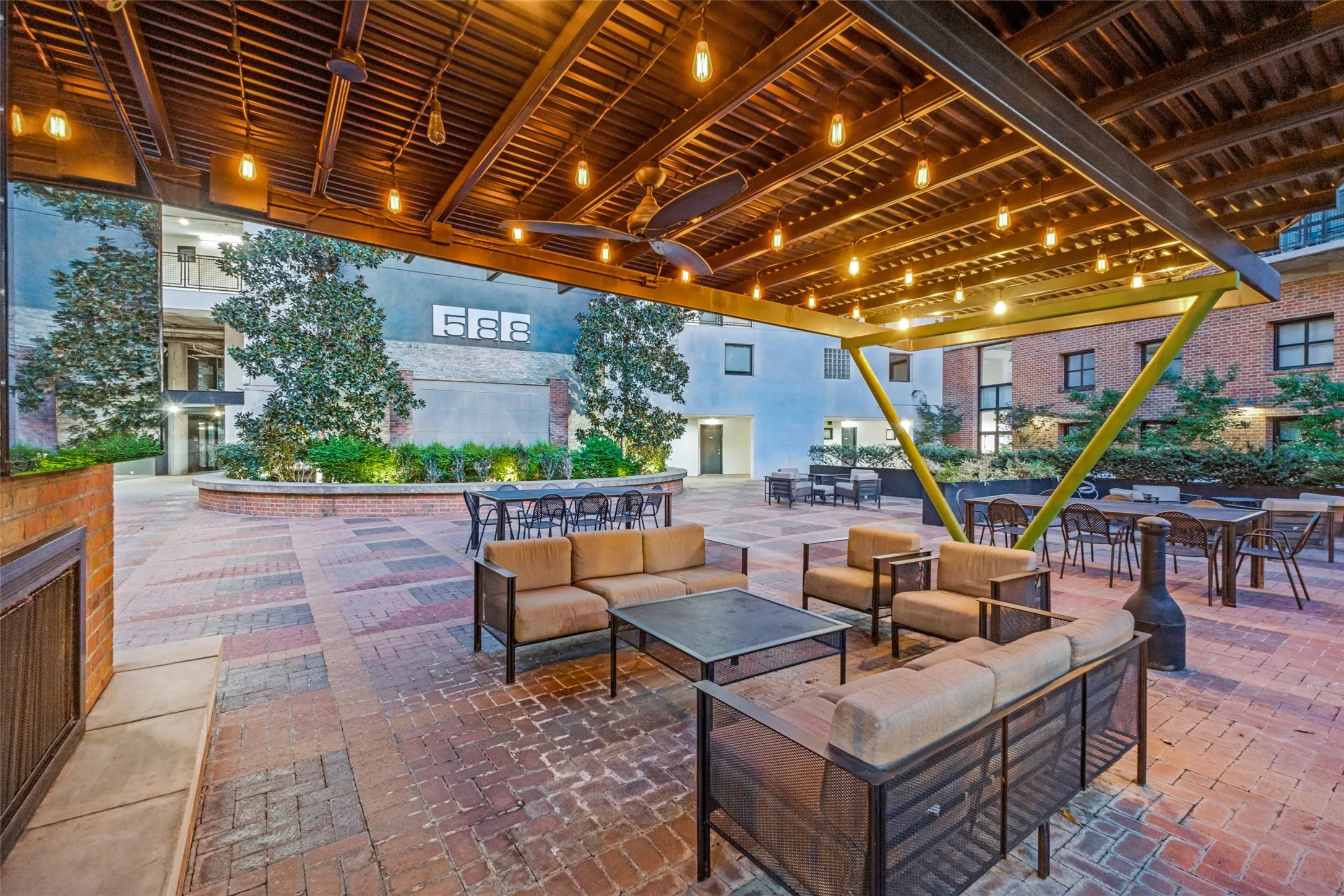 Expansive covered courtyard featuring a wood-beam ceiling with integrated lighting, brick and stone pavers, and multiple seating areas with built-in benches and tables