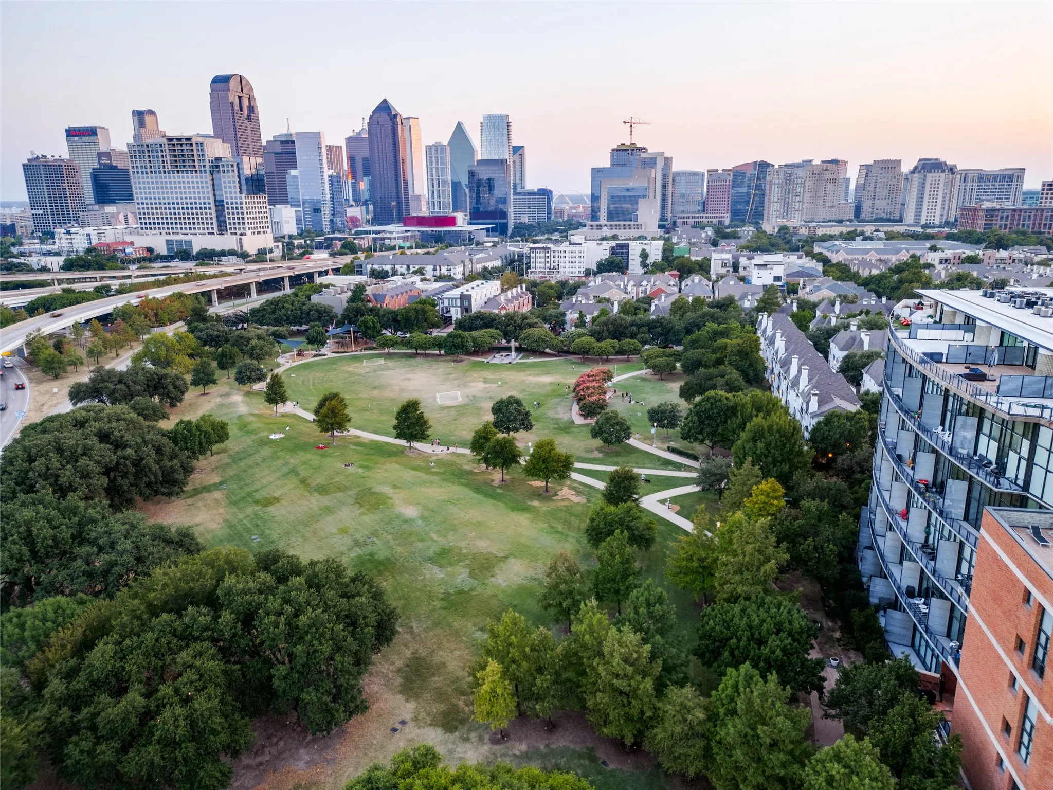 Expansive green space with mature trees, bordered by multi-story residential buildings and an urban skyline