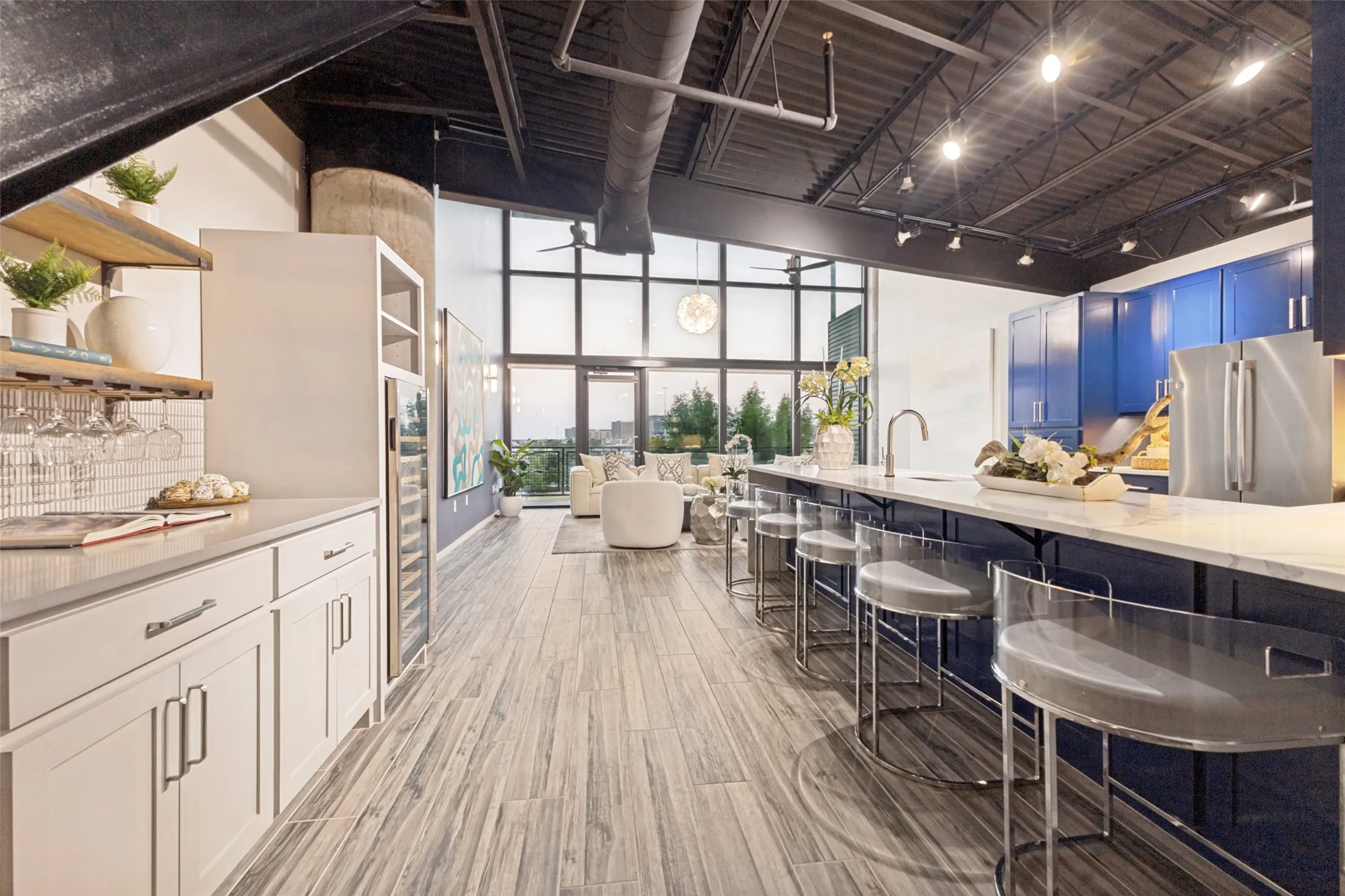 Kitchen featuring blue cabinetry, stainless steel appliances, white patterned countertops, wood-finish flooring, and exposed industrial-style ceiling elements