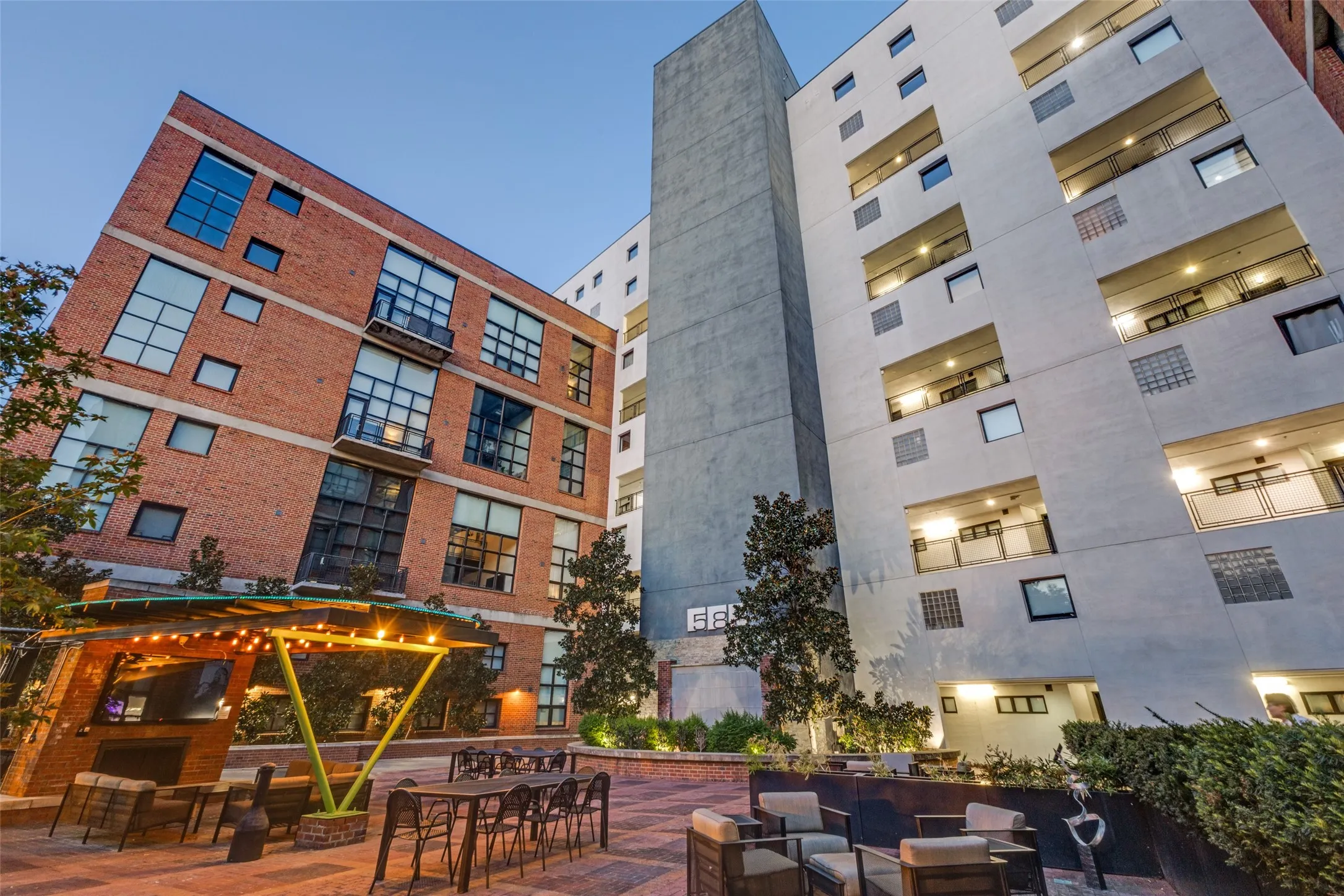 Paved courtyard featuring a pergola with string lights, a built-in outdoor fireplace, and multiple seating areas